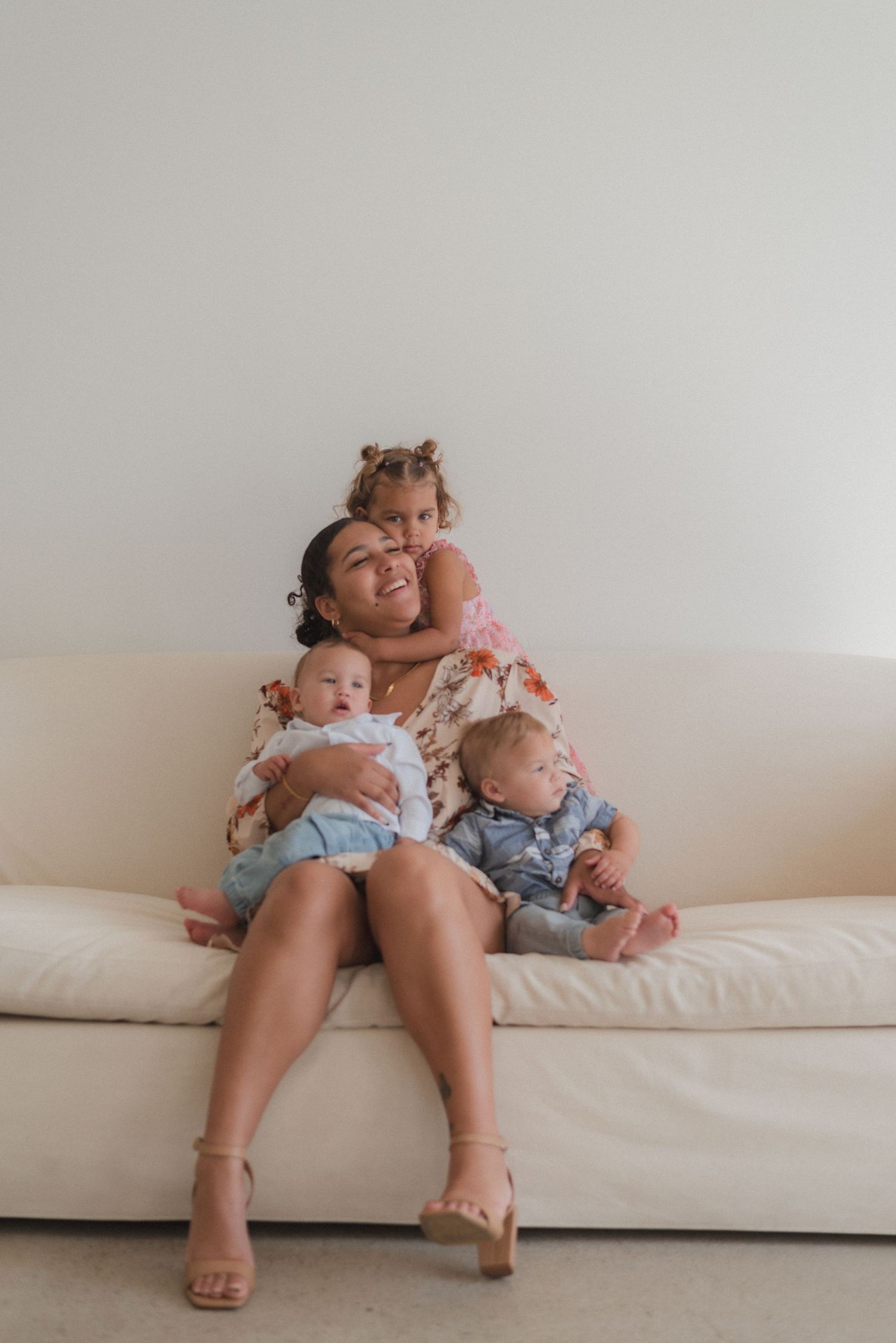 Intimate family moment captured on white couch with natural lighting and minimal decor.