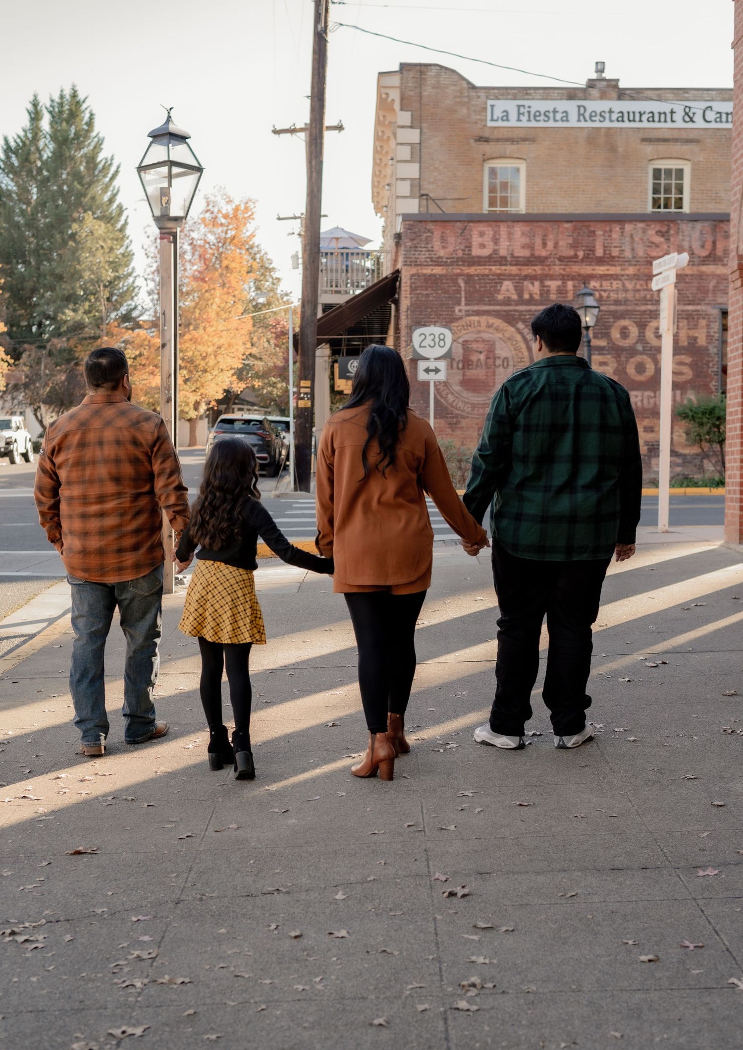 Family walking together on a sidewalk past vintage brick buildings in fall.
