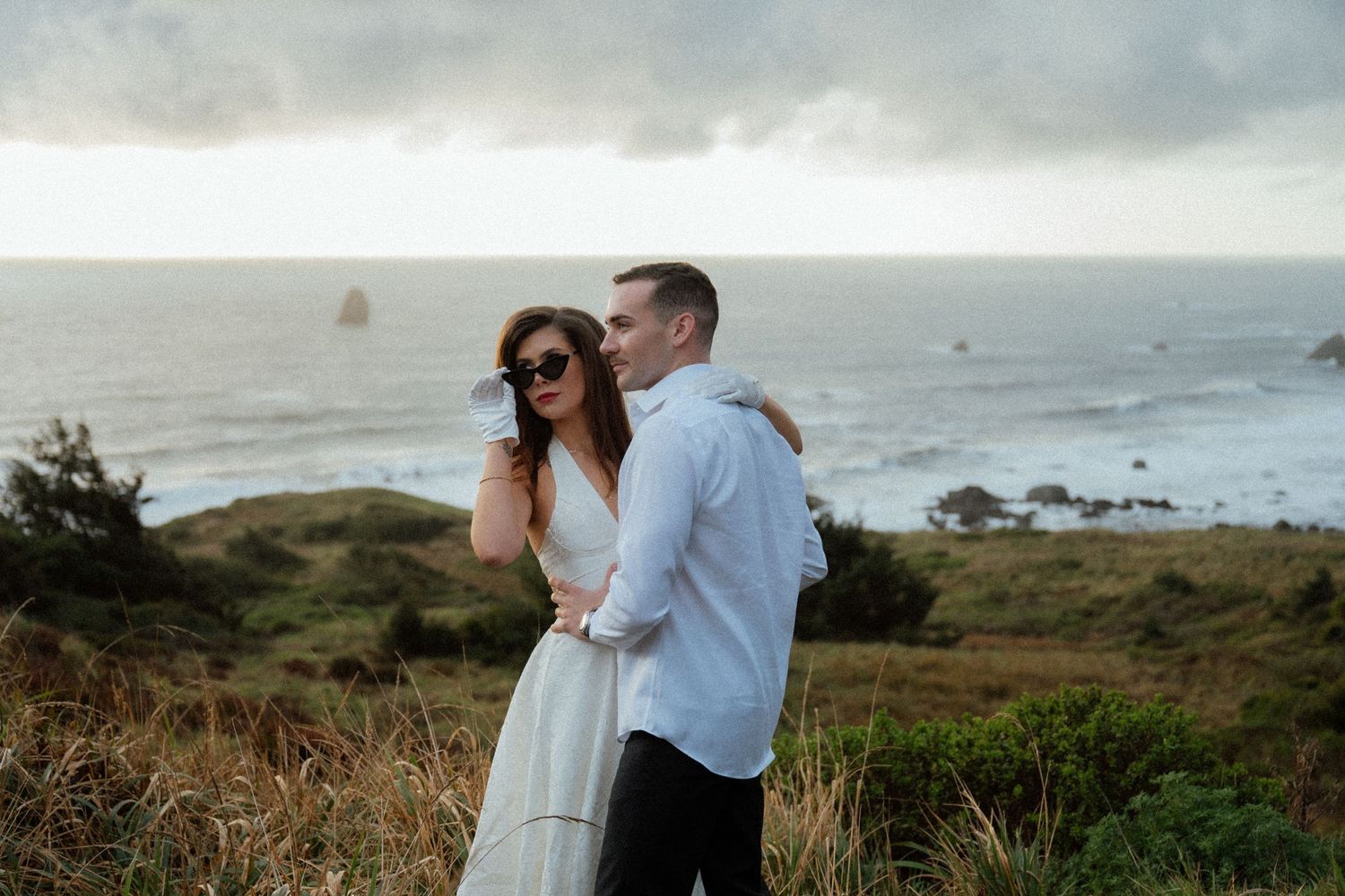 Couple enjoys scenic coastal view on cloudy day along rugged shoreline.