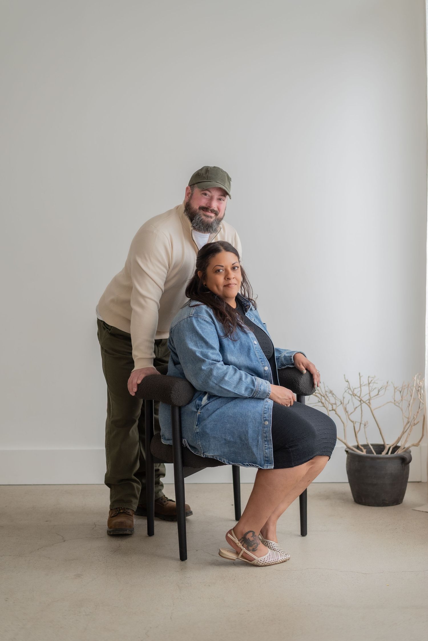 A couple poses playfully in a minimalist studio with white walls and wooden furniture.
