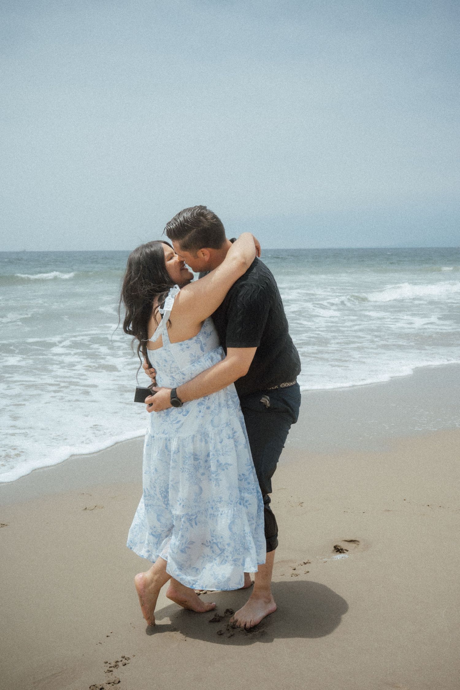 A romantic embrace on the beach with waves rolling in on an overcast day.