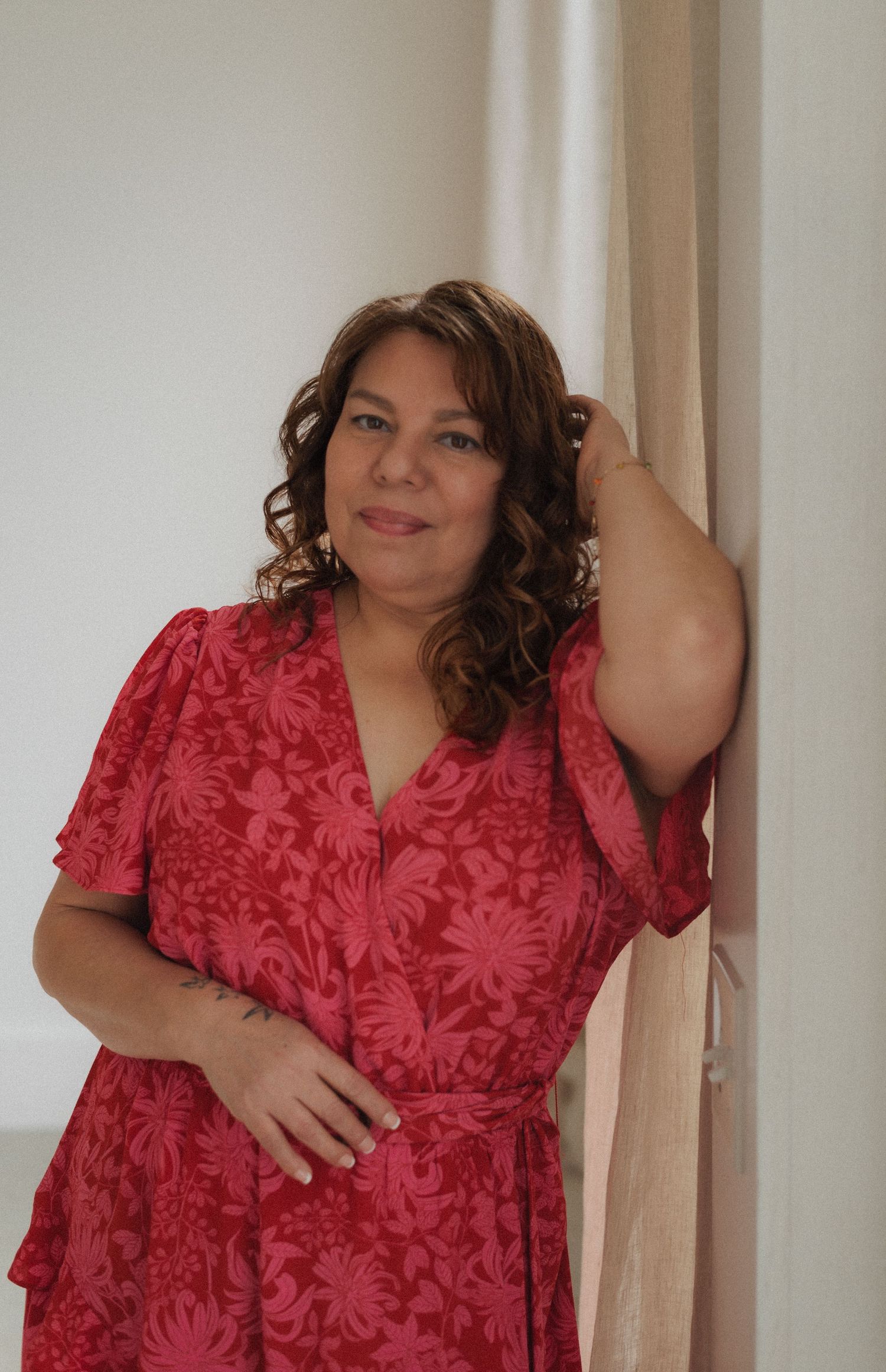 Woman in red floral dress poses confidently against a white wall.