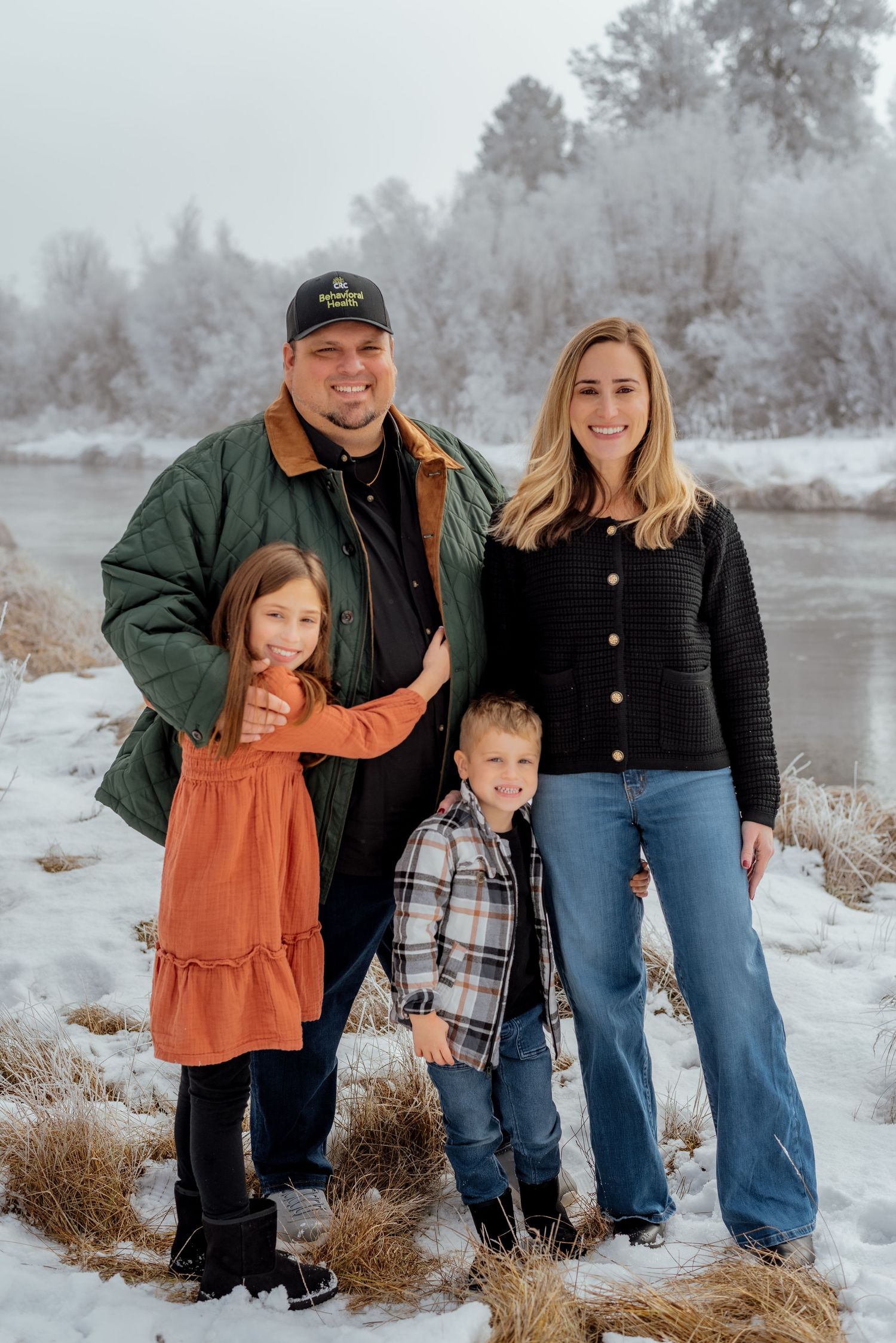 Family wearing coordinated casual outfits poses together in snowy winter setting.