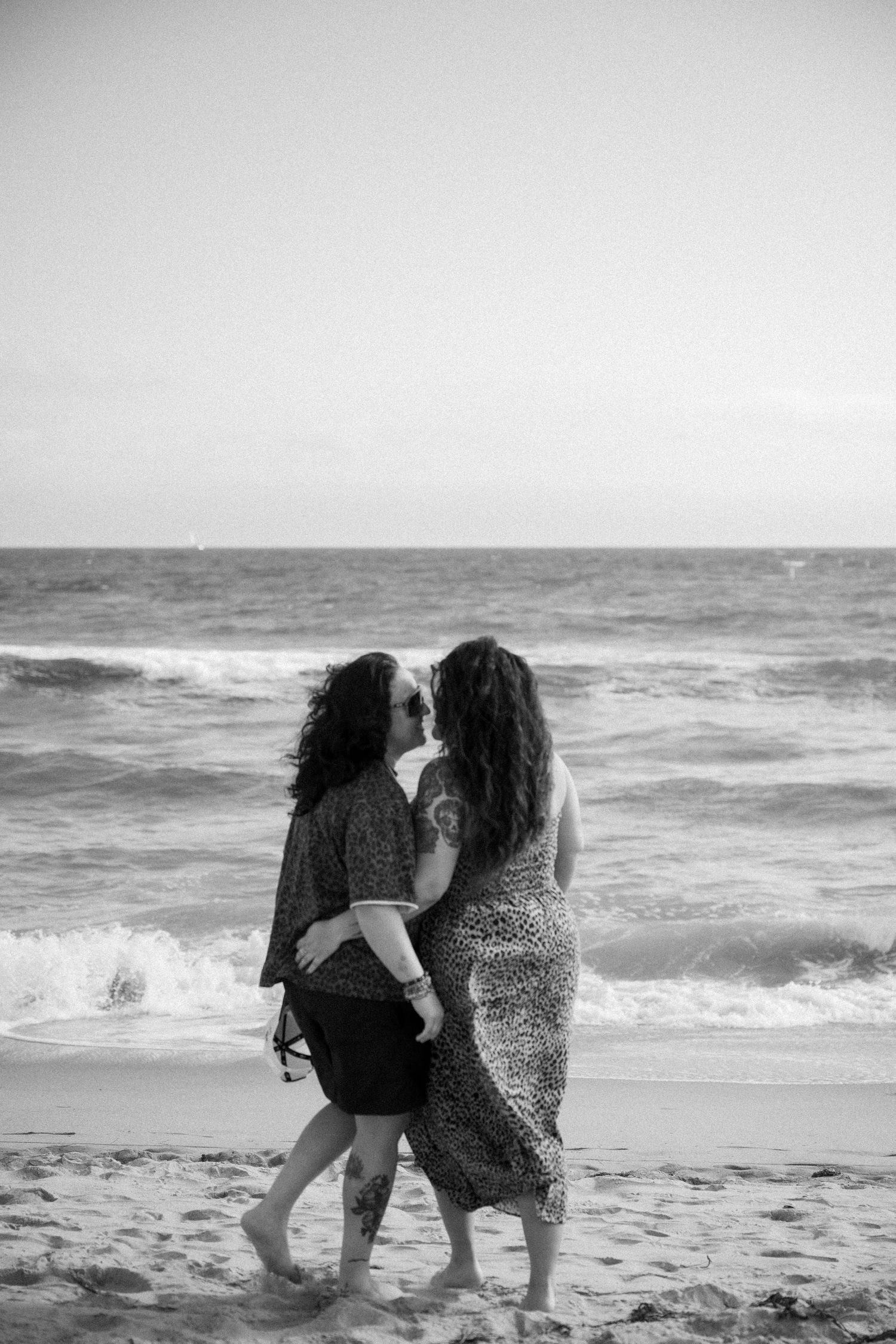 Two people walking together on a beach with waves crashing in the background.