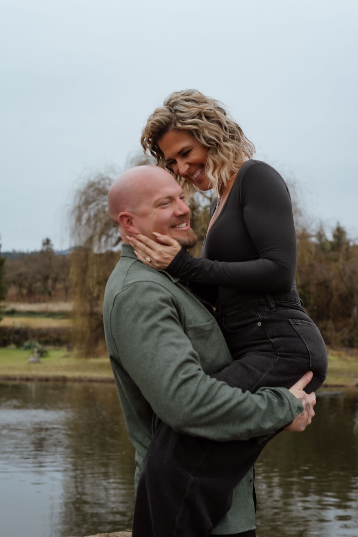 Intimate moment captured between couple by a serene lake during a cloudy afternoon.