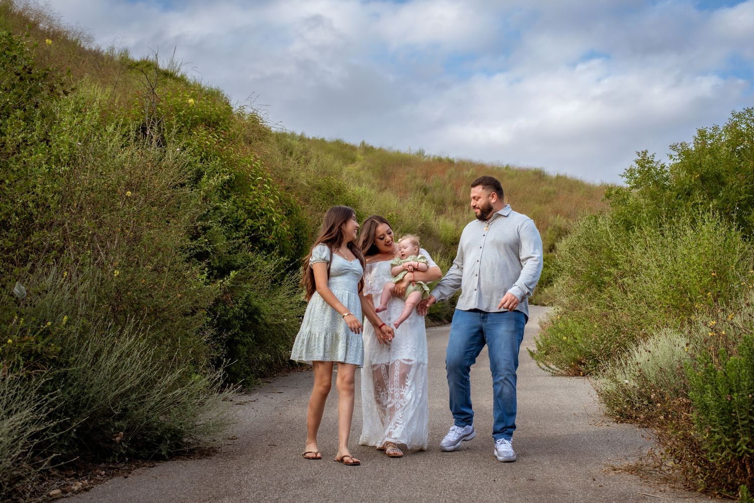 A family walks together on a dirt path surrounded by green hillside vegetation.