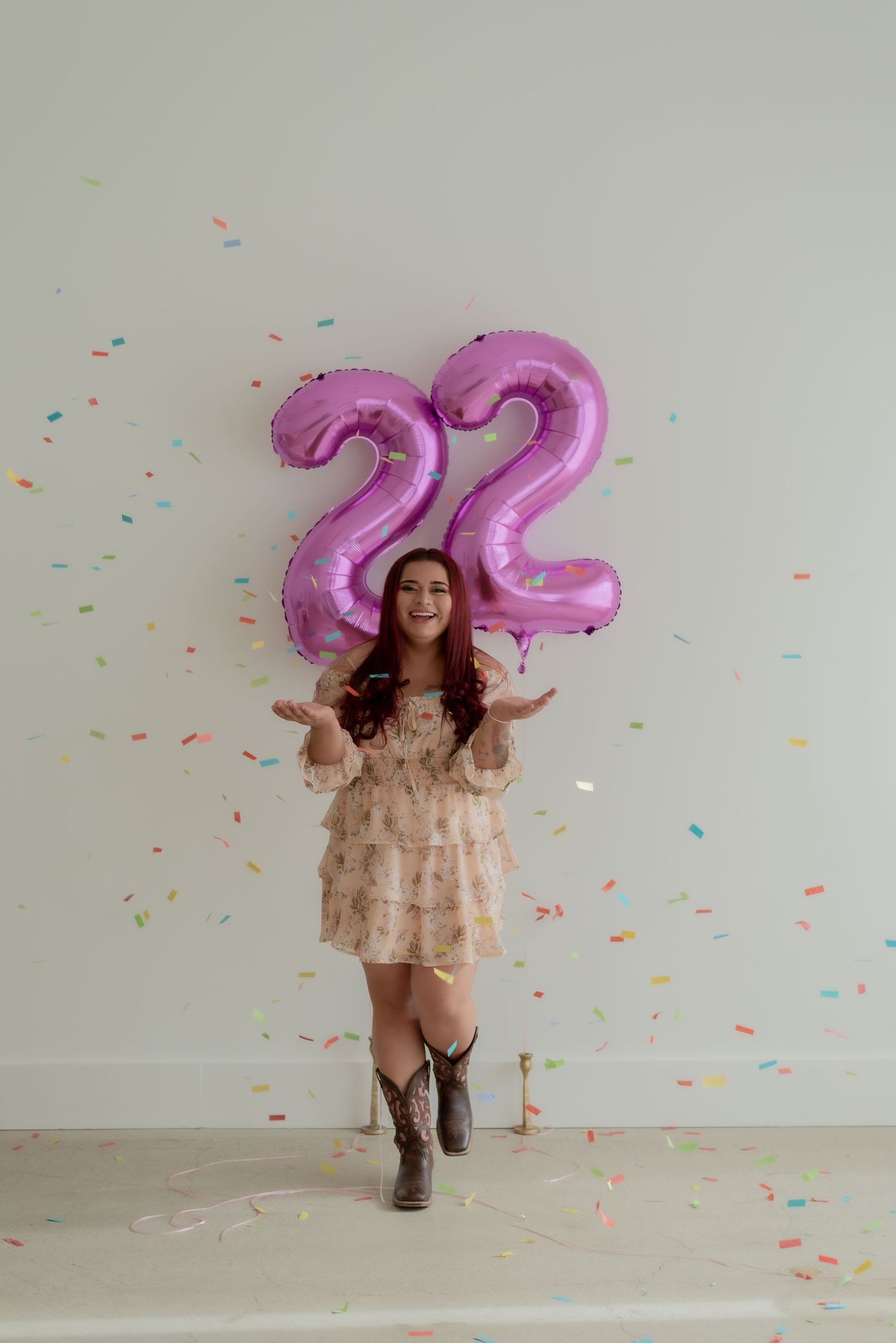 A celebratory scene with pink number 22 balloons and confetti against a white wall.