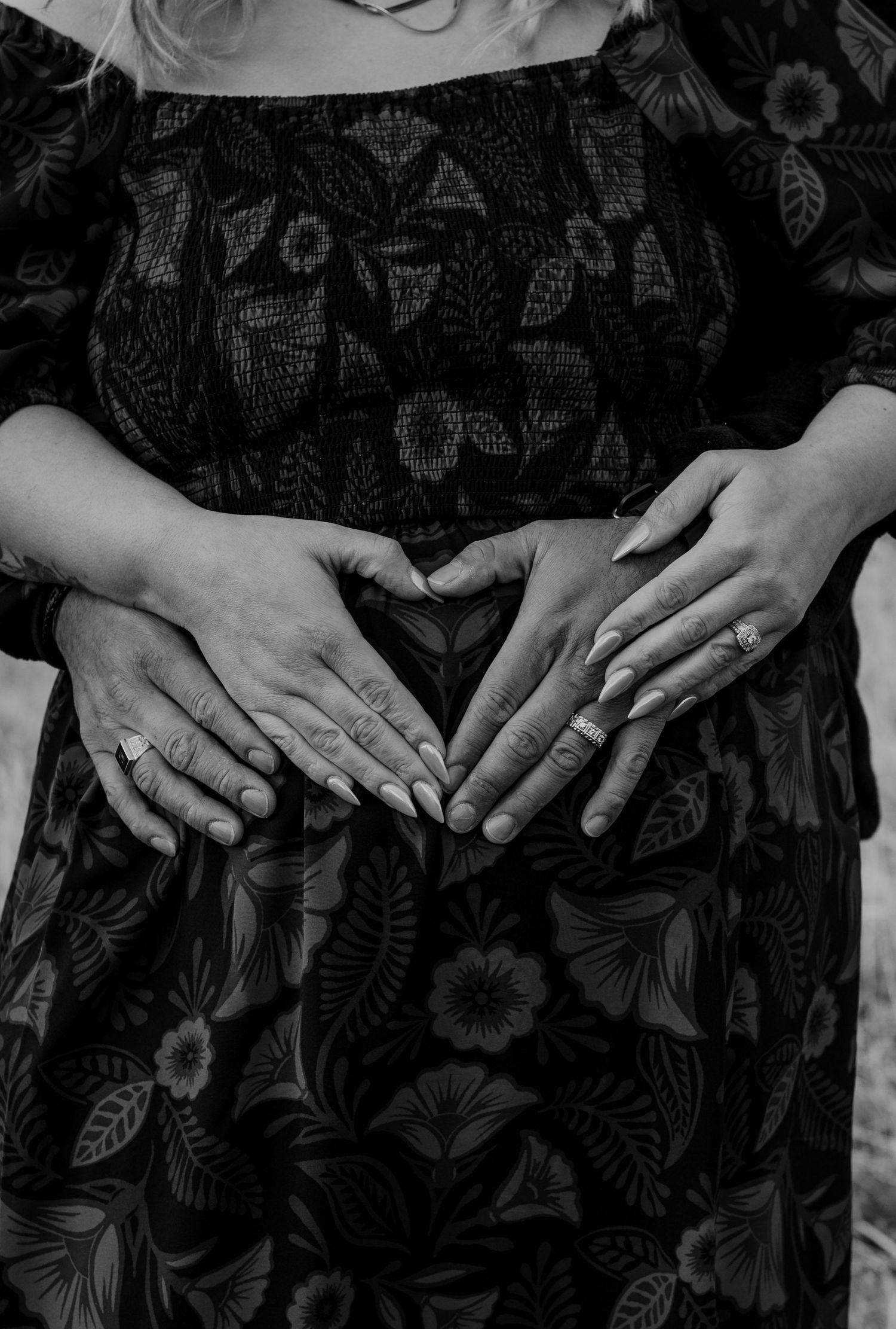 Multiple hands forming a heart shape over a floral patterned dress in black and white.