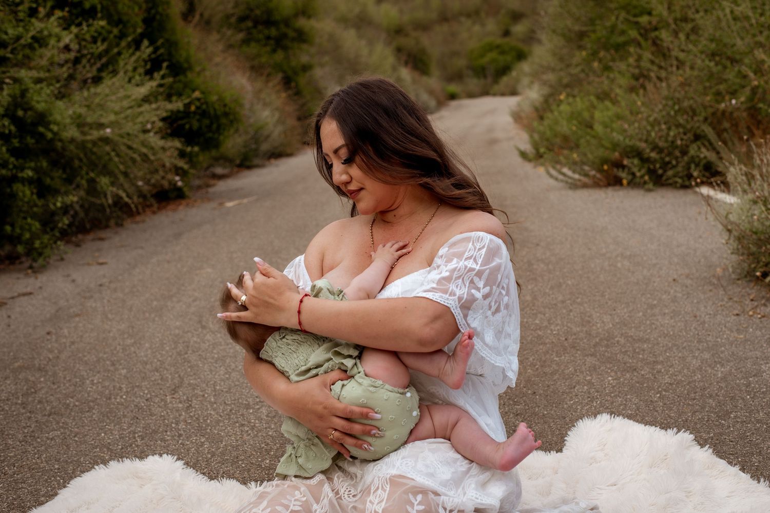 An intimate motherhood moment captured on a white blanket outdoors.