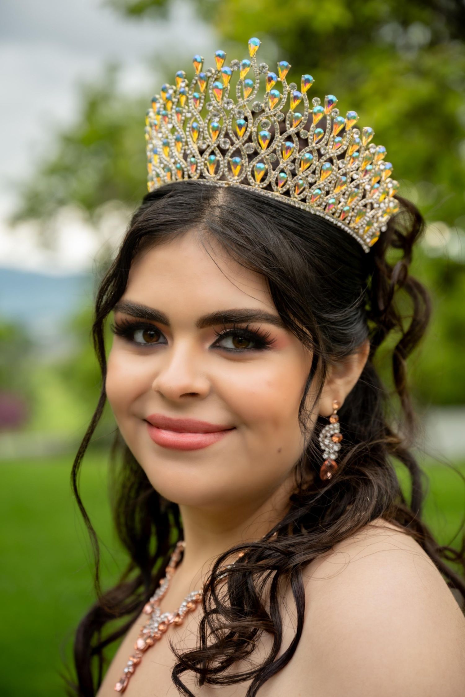 Sparkling gold crown and elegant makeup details captured in an outdoor portrait.