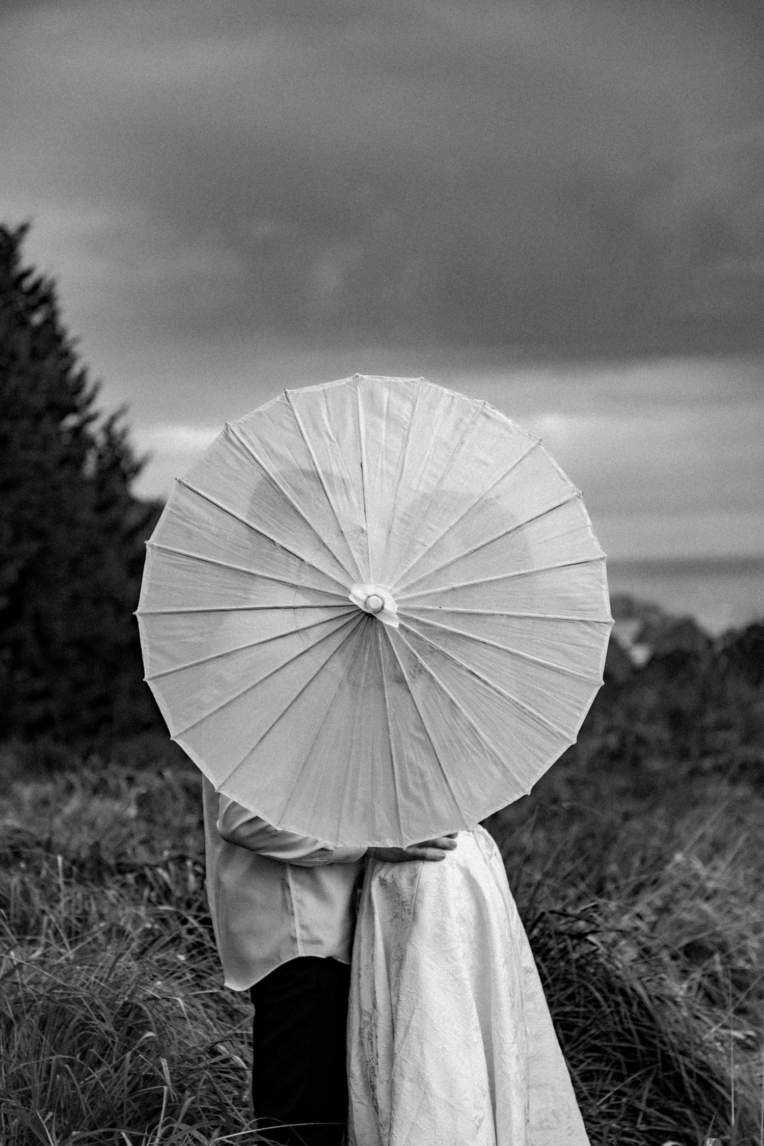Artistic black and white photos featuring white parasols against a moody sky.