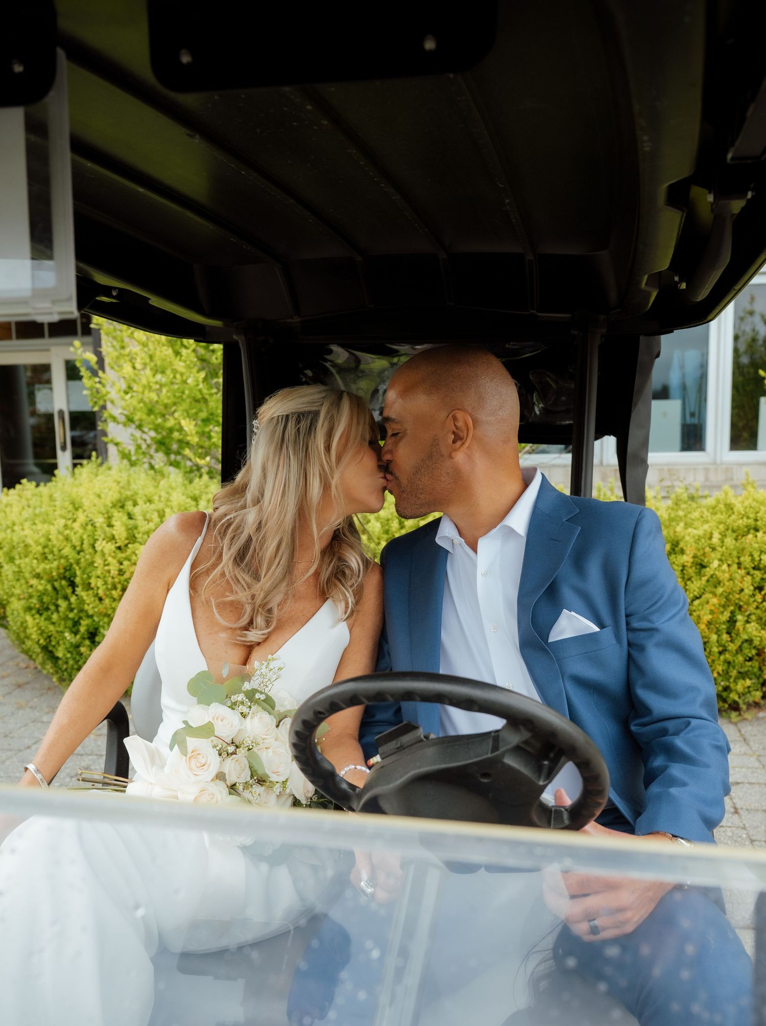 A couple shares tender moments while riding in a golf cart on their wedding day.