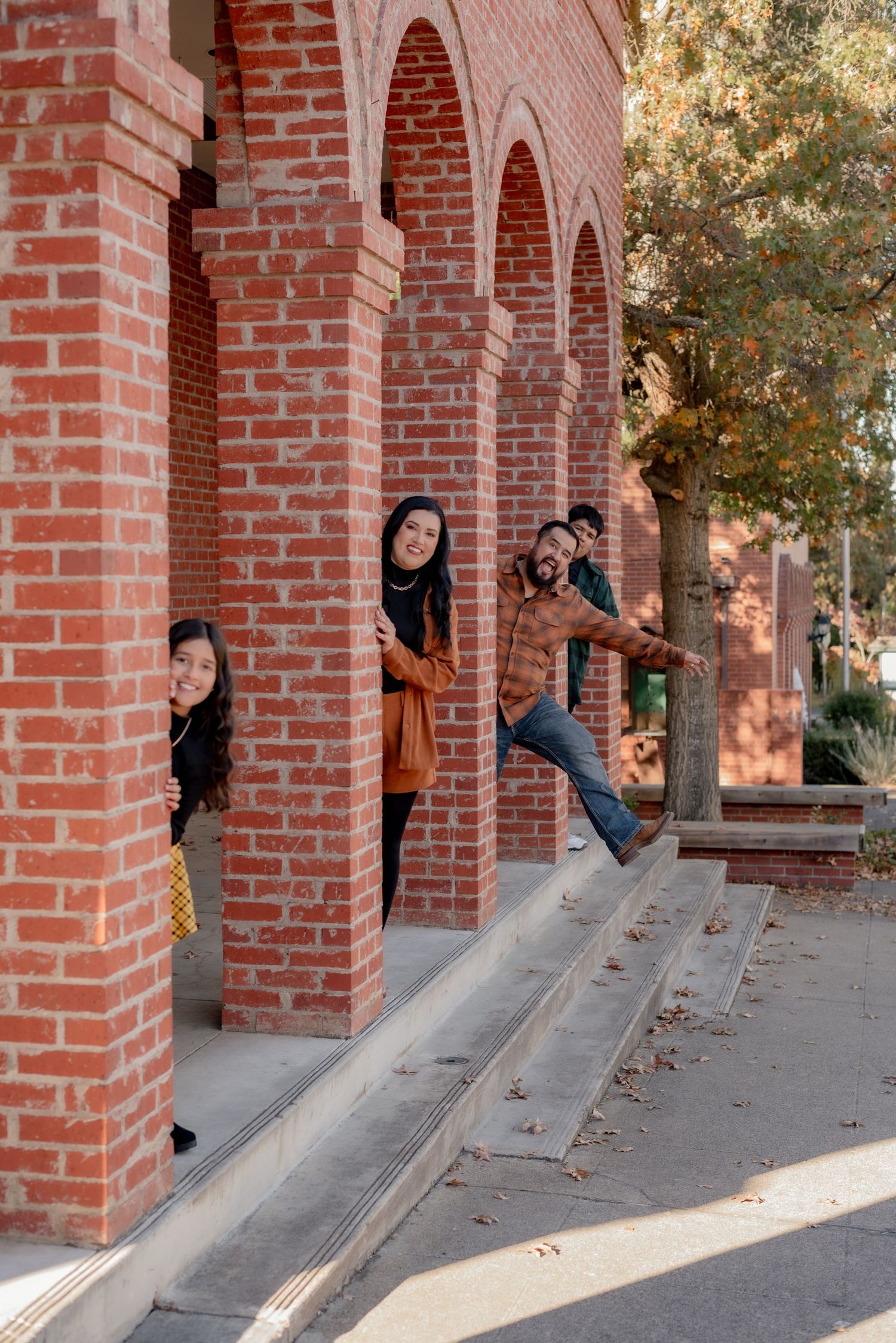 Fun sequence of people peeking out from behind red brick columns in an outdoor setting.