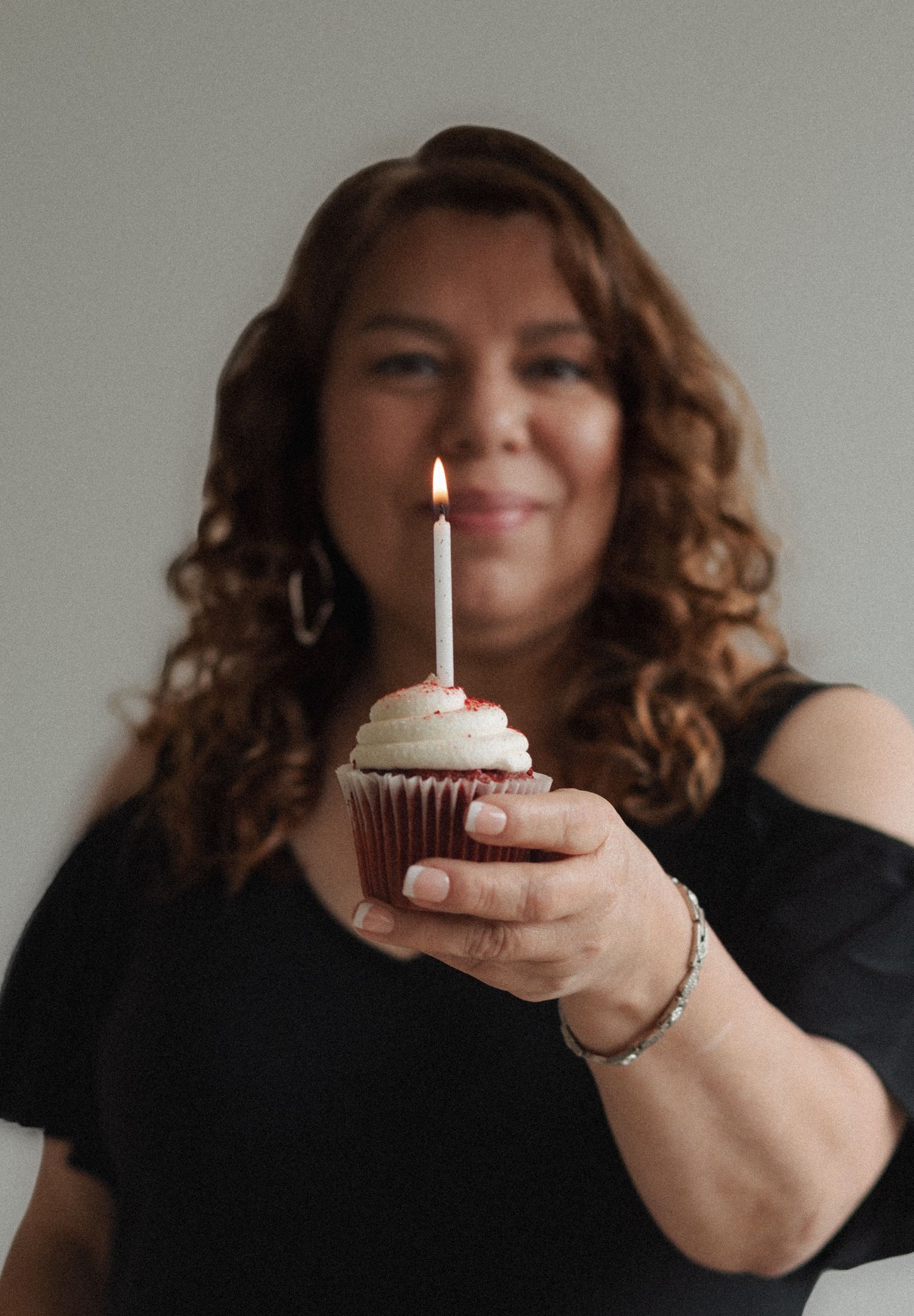 Person holding a lit birthday cupcake with candle in black outfit.