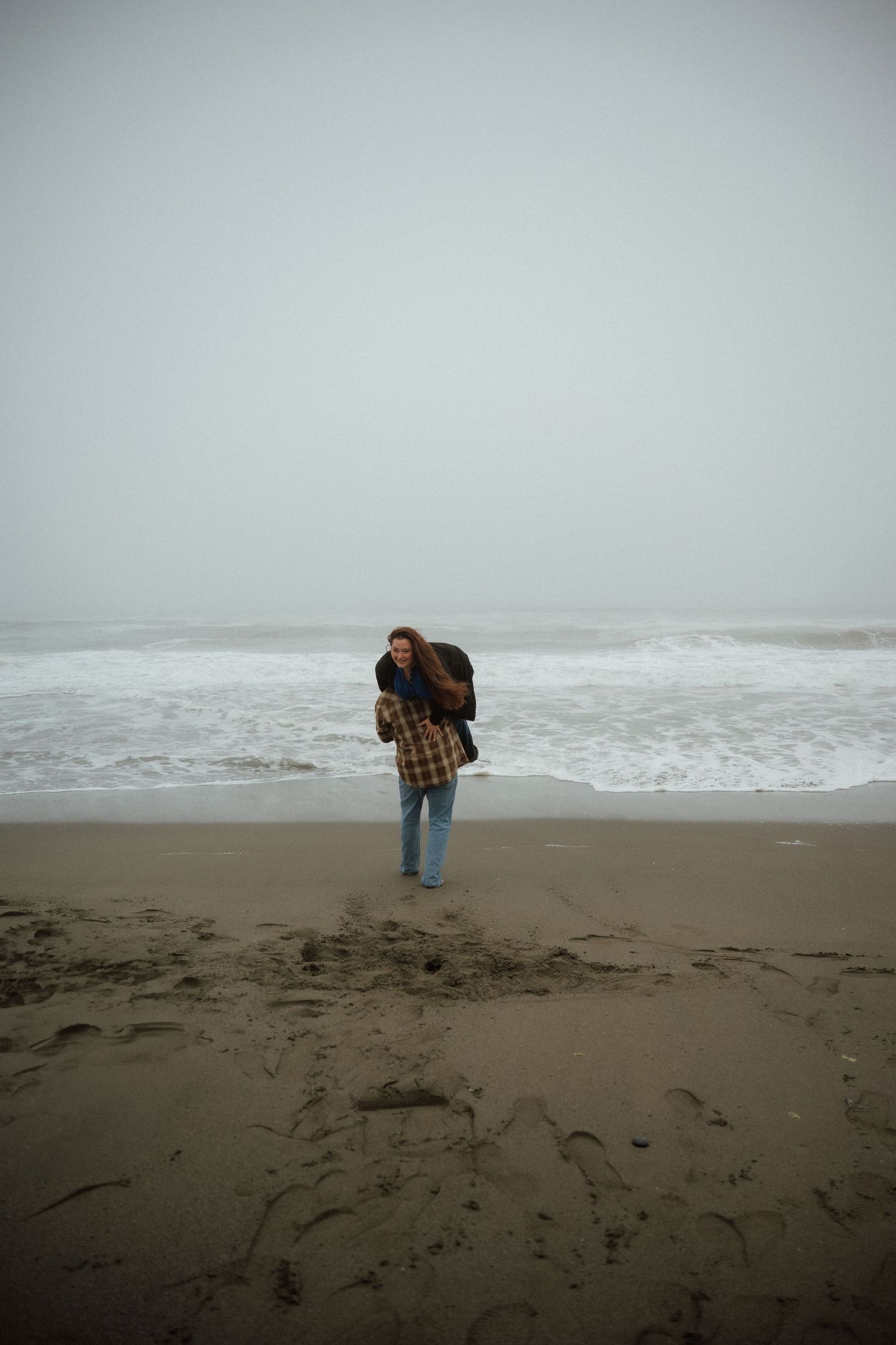 Figure walks along misty beach shoreline collecting items from the sand.