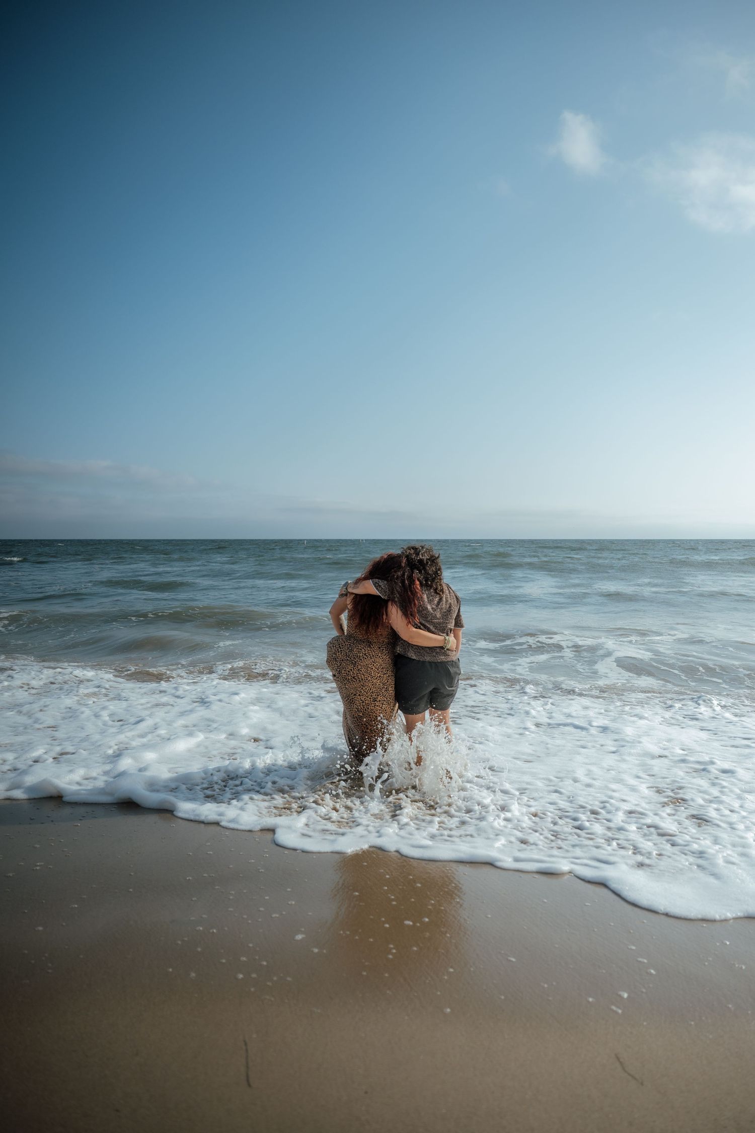 A couple embracing in the ocean waves as water splashes around them on a sunny beach day.