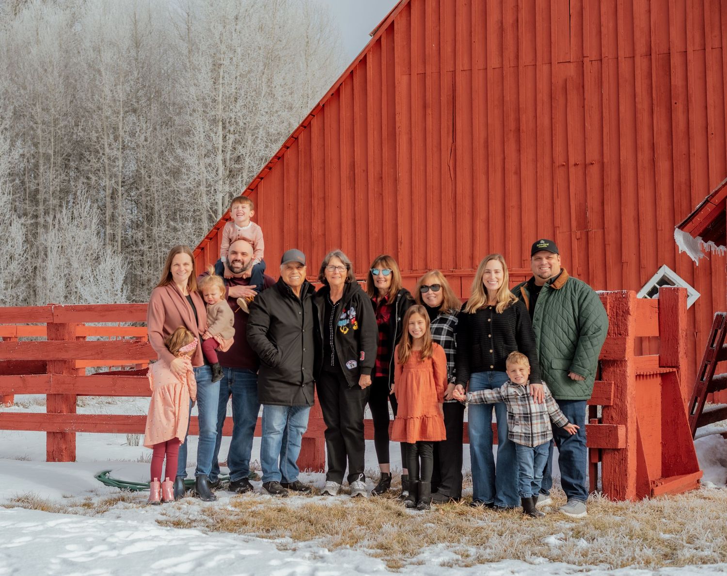 Large group poses for photos in front of a bright red barn in winter.