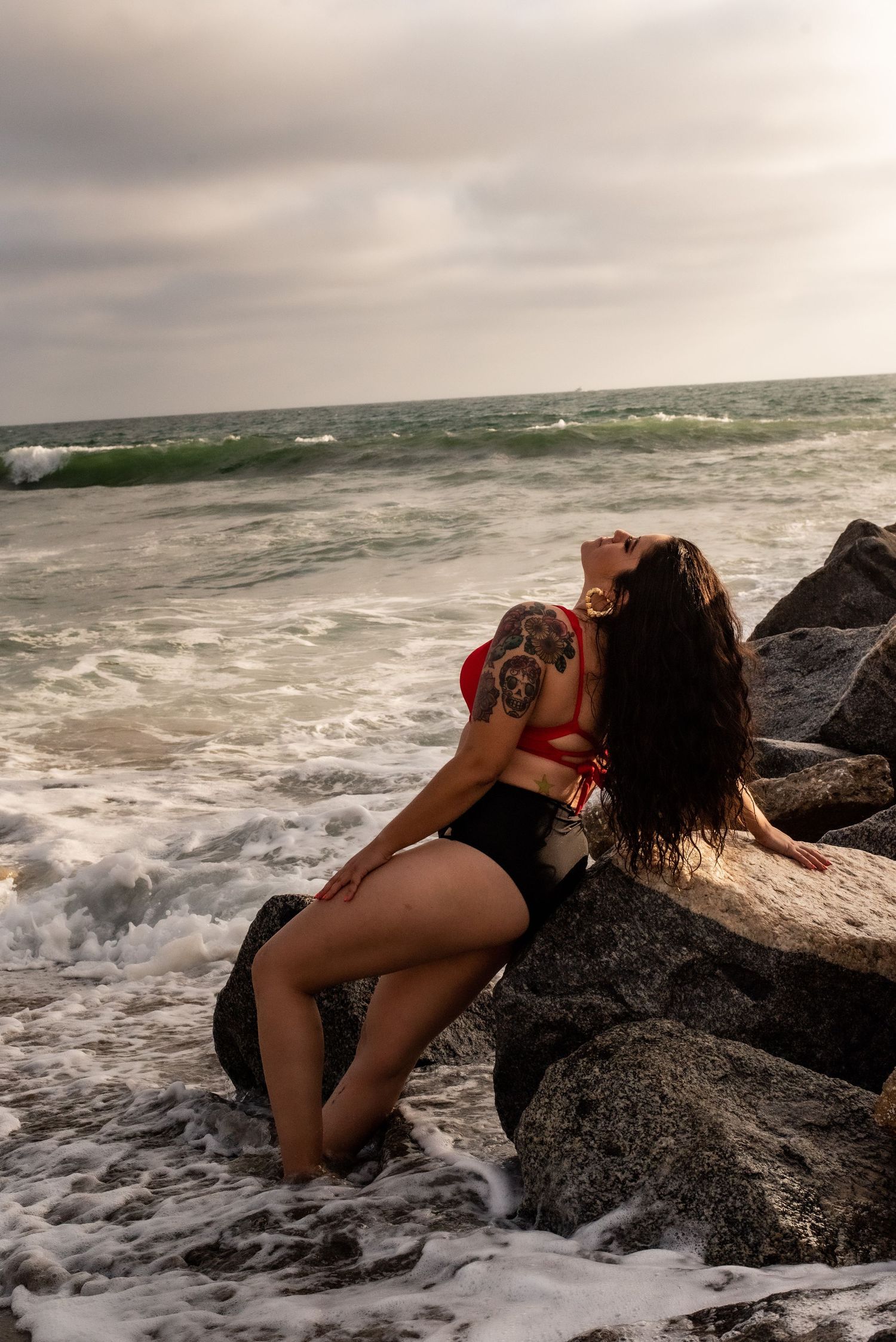 Dramatic oceanside photo session on dark rocks with crashing waves in background.