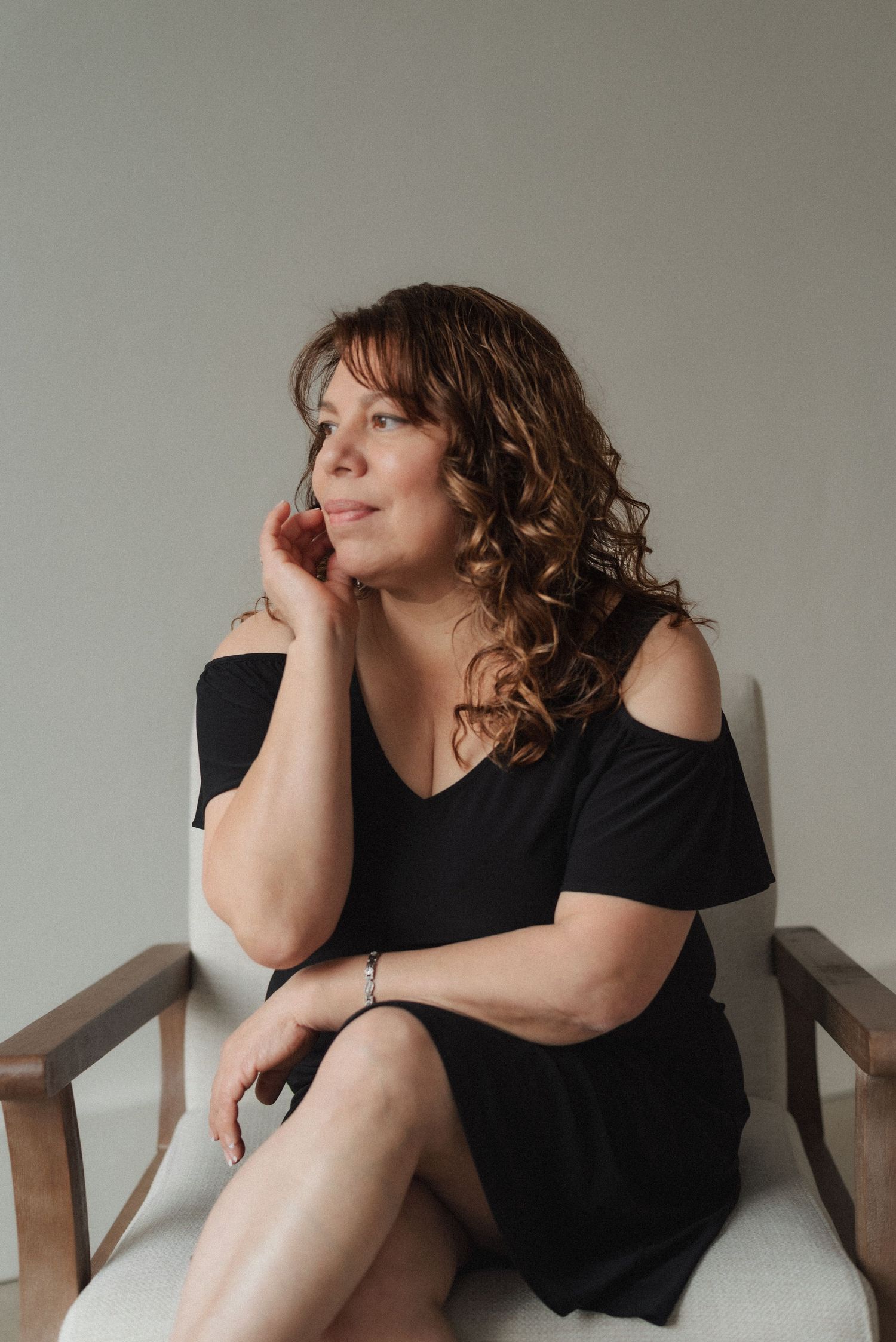 Person in black dress reclining thoughtfully on wooden chair.