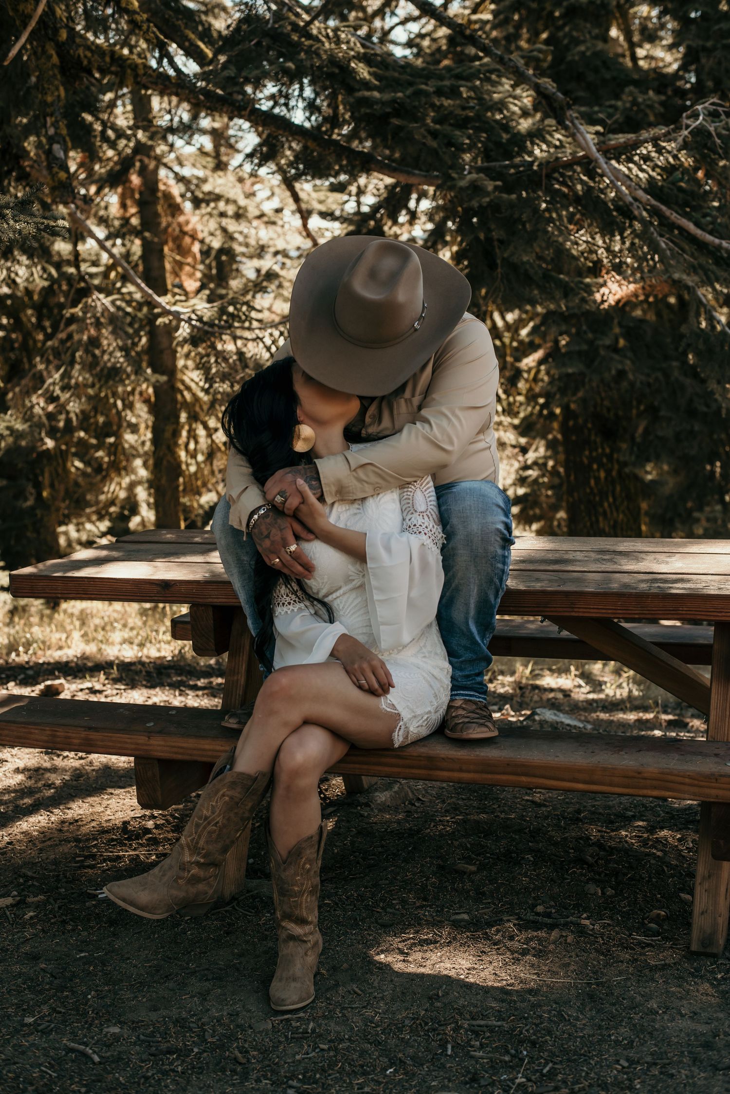 A romantic scene unfolds on a wooden bench surrounded by pine trees at sunset.