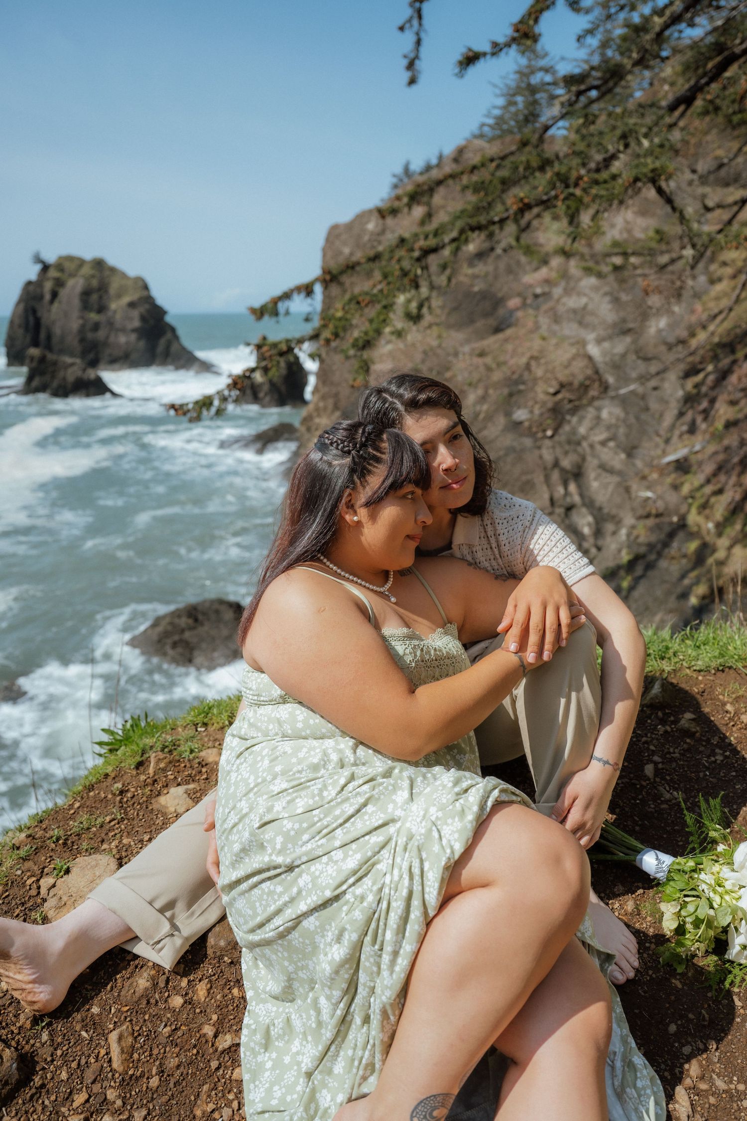 Two people in light summer clothing embrace on a cliff overlooking the Pacific ocean.