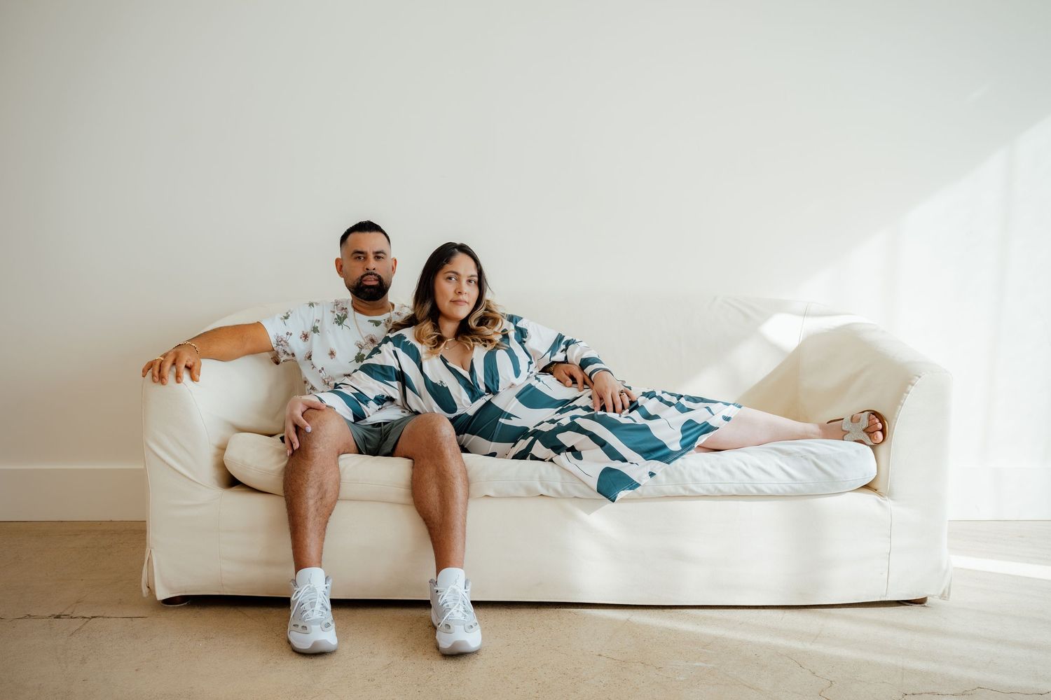 Two people relax on a white sofa wearing coordinated blue and white tie-dye clothing.