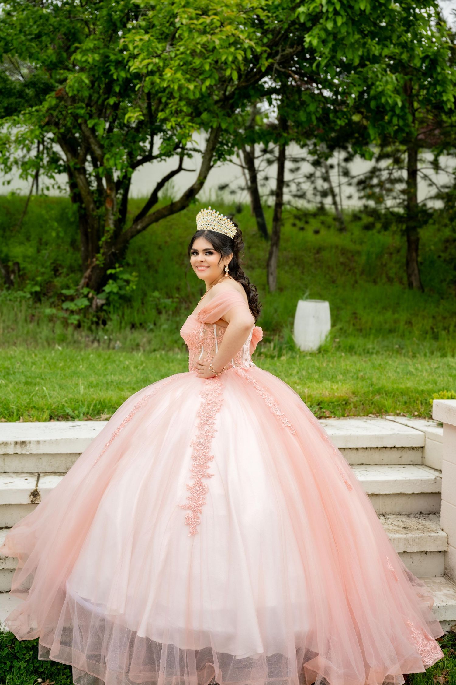 A flowing pink quinceañera dress with layered tulle skirt photographed in an orchard setting.