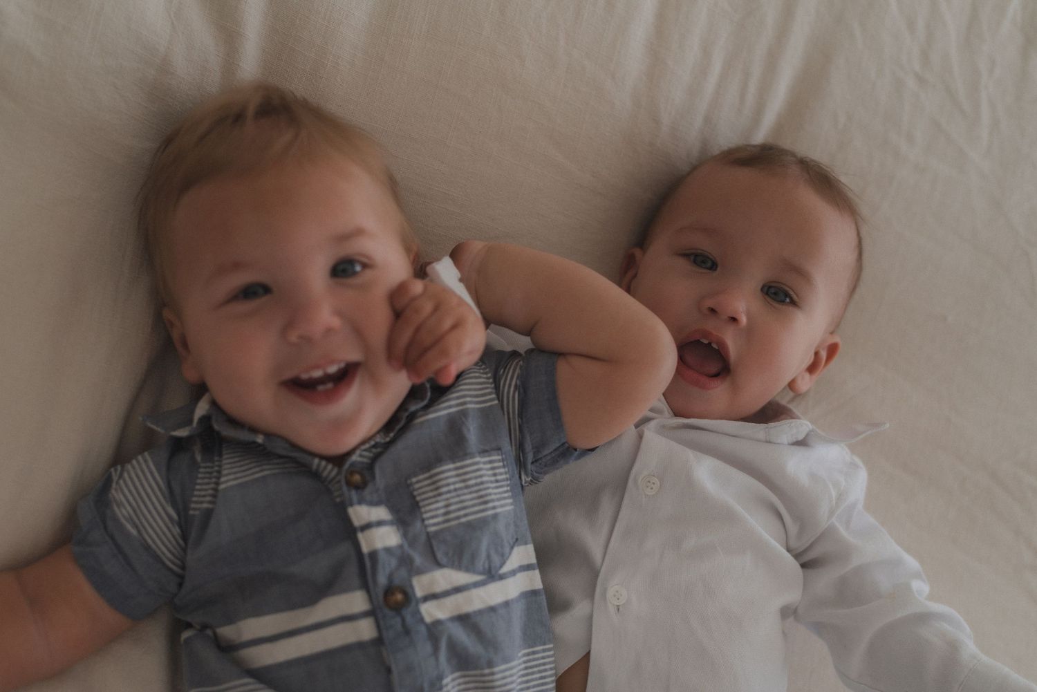 Sweet candid moment of infants lying together on a white couch sharing smiles and laughter.