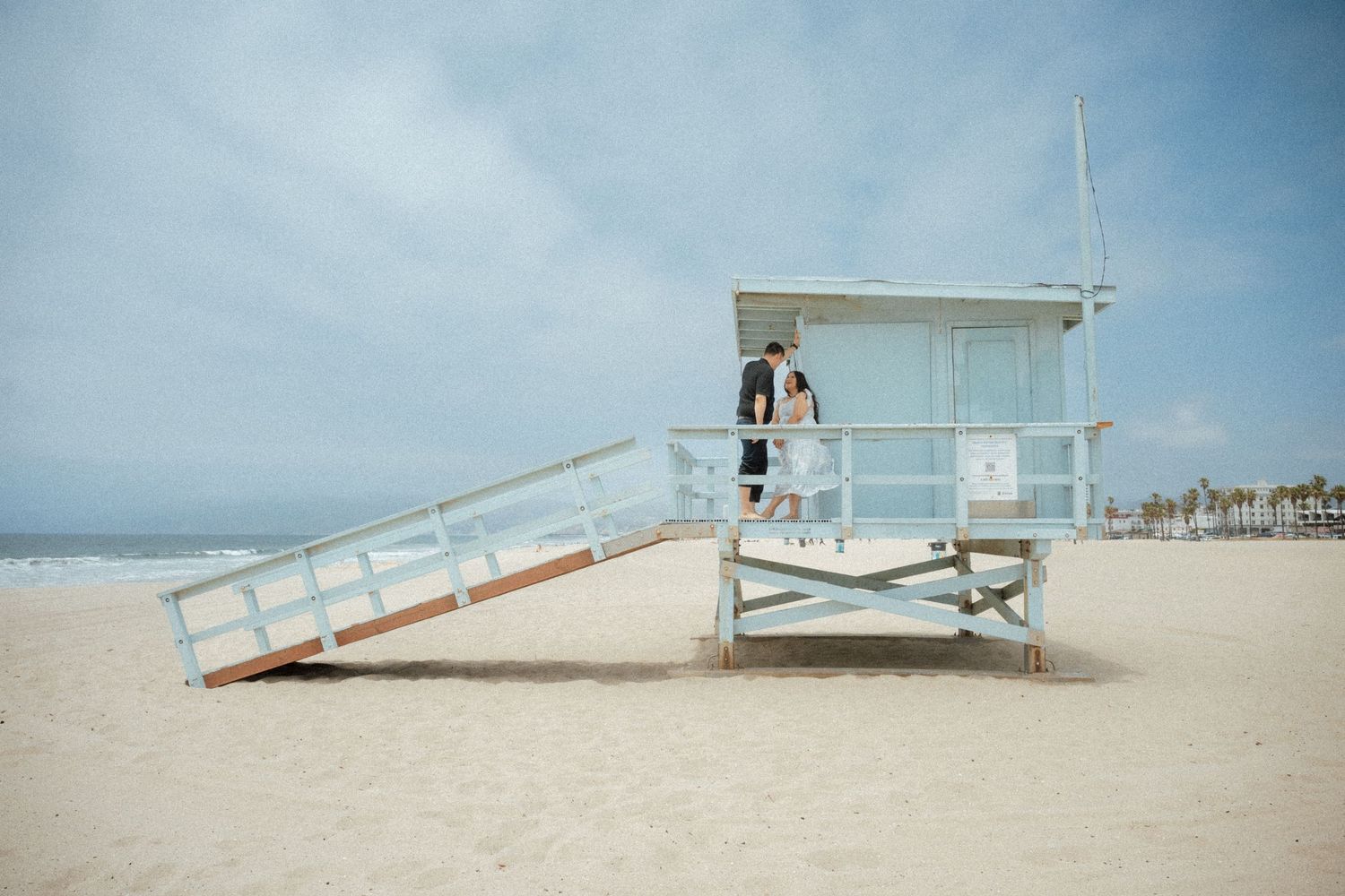 A row of white lifeguard towers on a sunny beach with waves in the background.