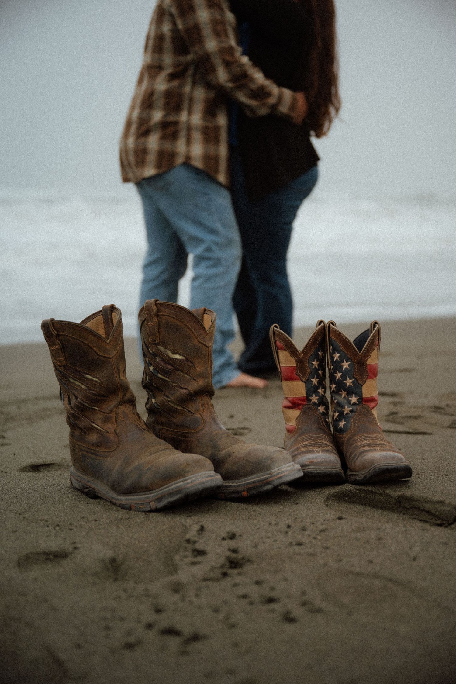 Three pairs of cowboy boots stand together on dark beach sand.