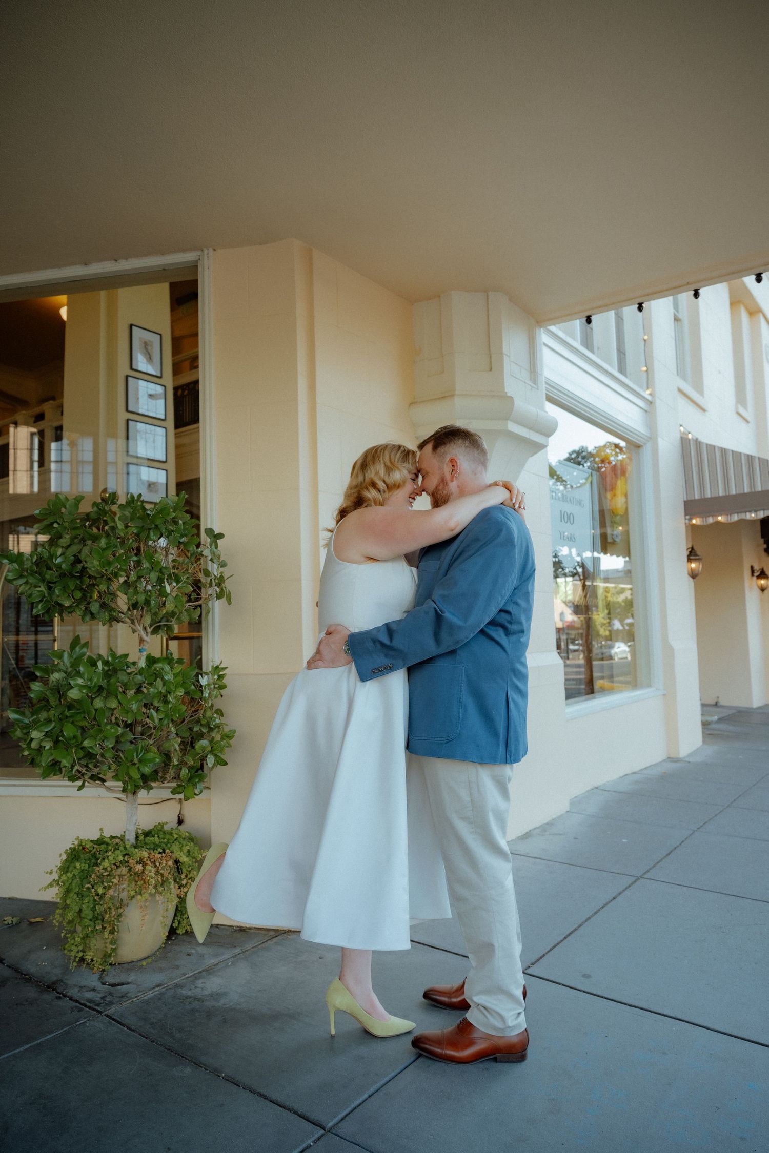Couple embracing on covered walkway with potted plants nearby.
