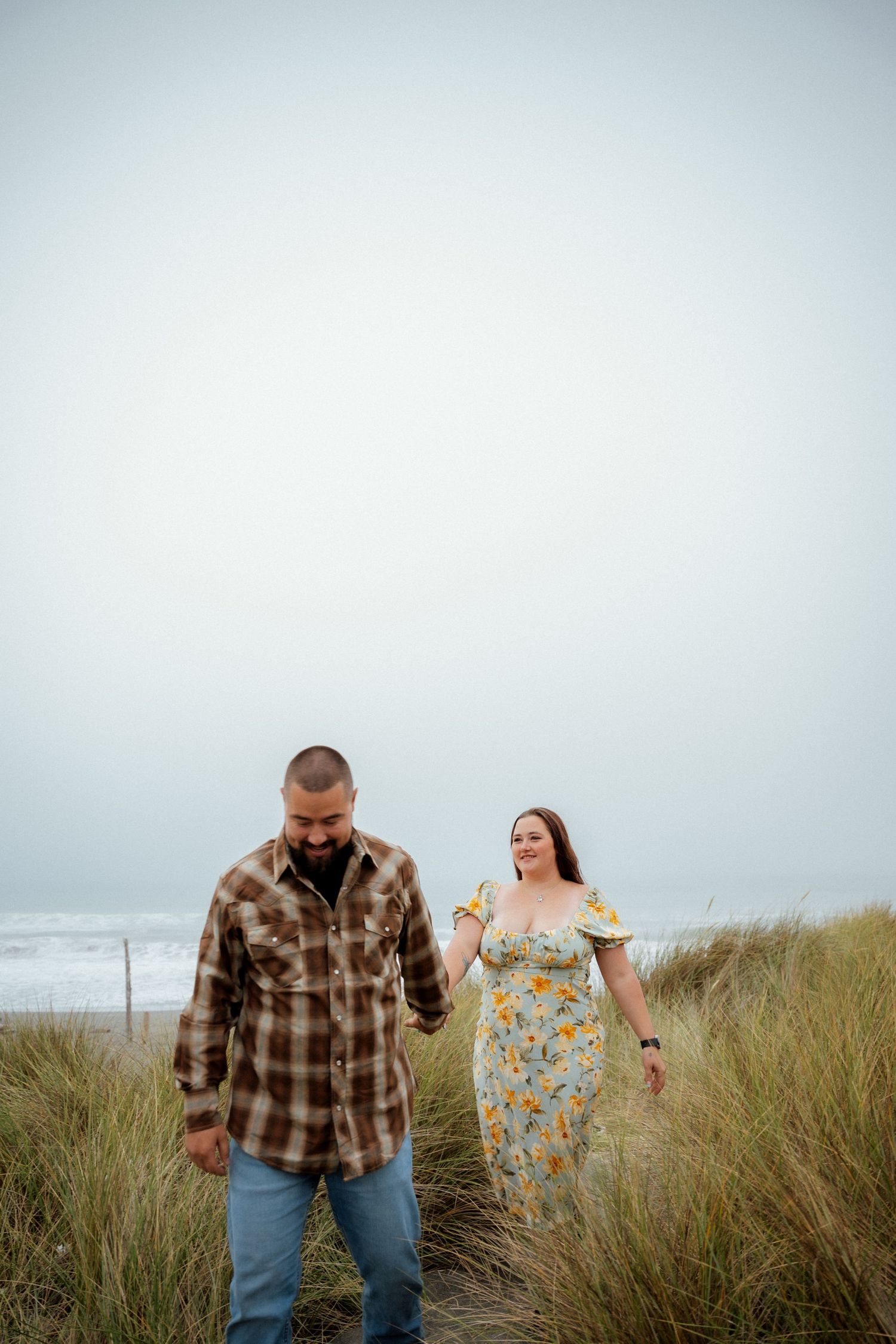 A couple explores a windswept coastal trail through tall beach grass.