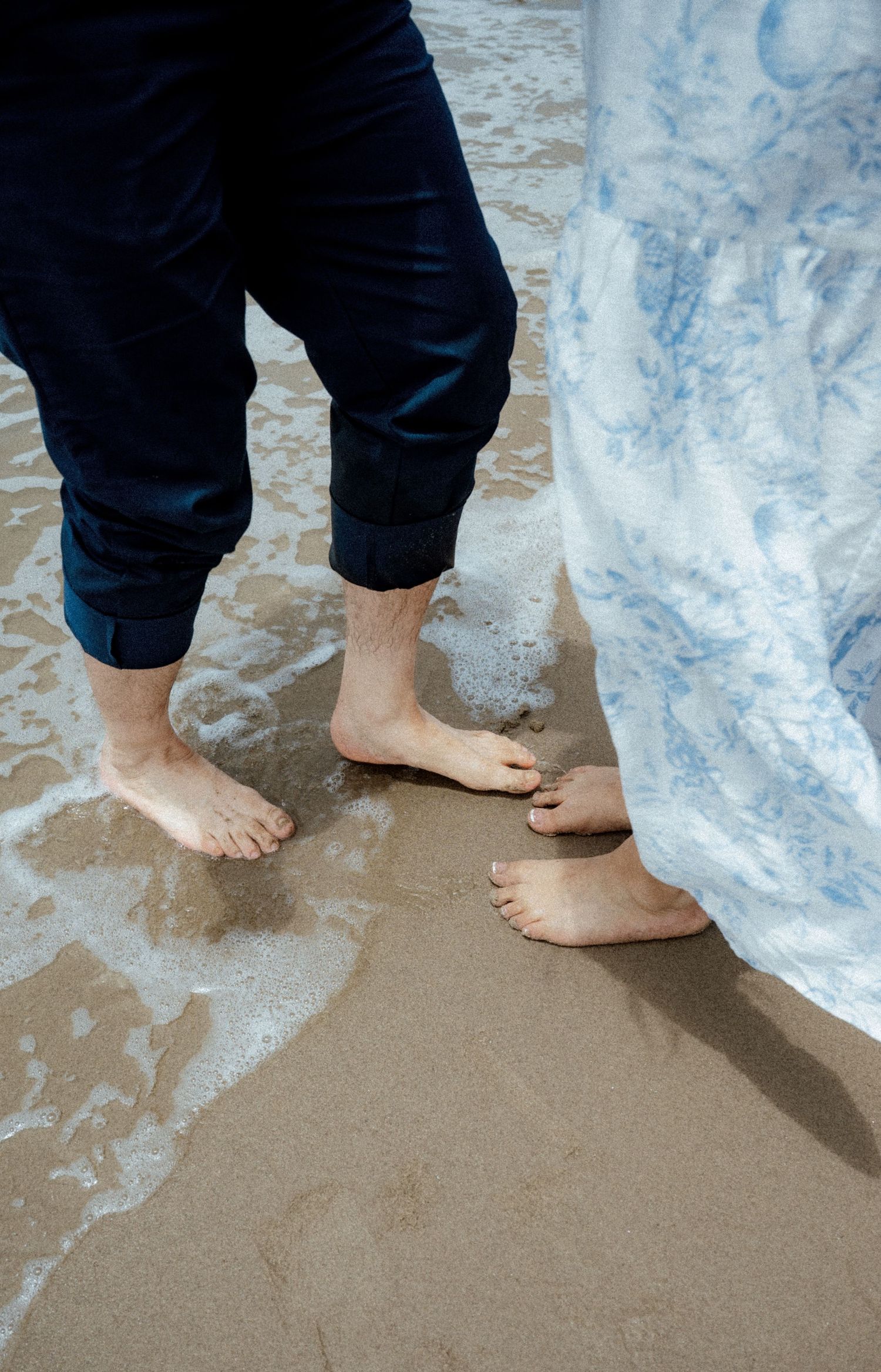 Bare feet standing in wet sand as ocean waves wash over them.