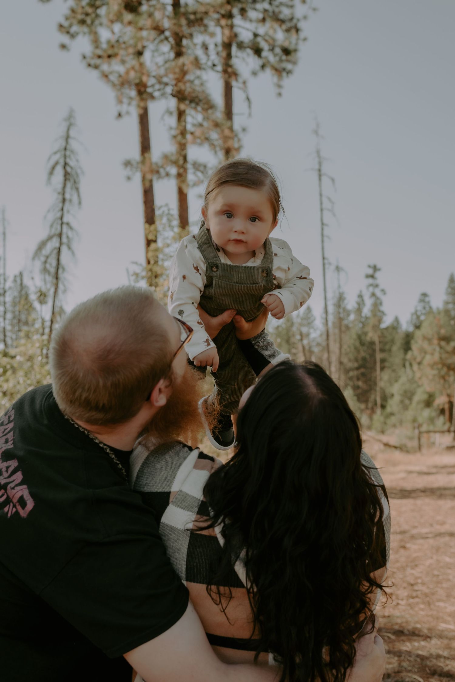 Candid family moment captured outdoors among pine trees.