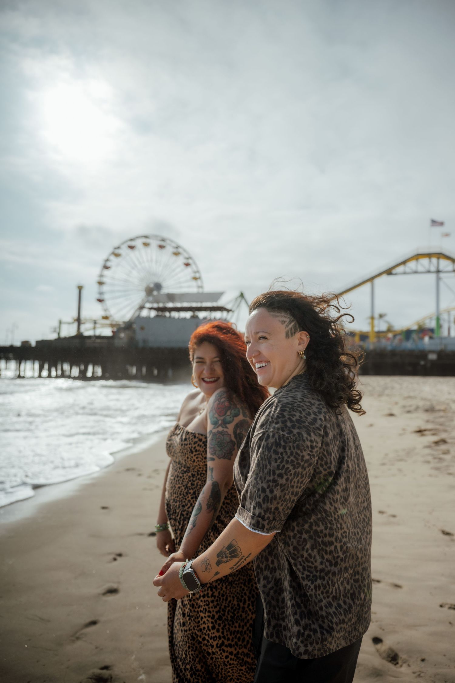 Two people sharing a joyful moment on the beach with an amusement park pier in the background.