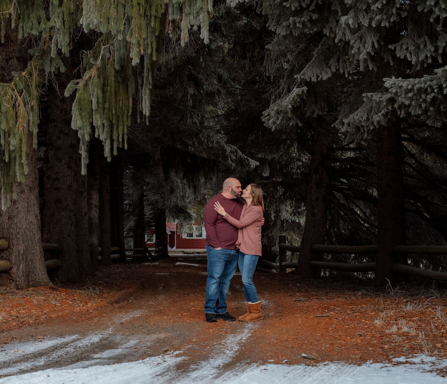 A couple embraces in a snowy forest setting with moss-covered trees.