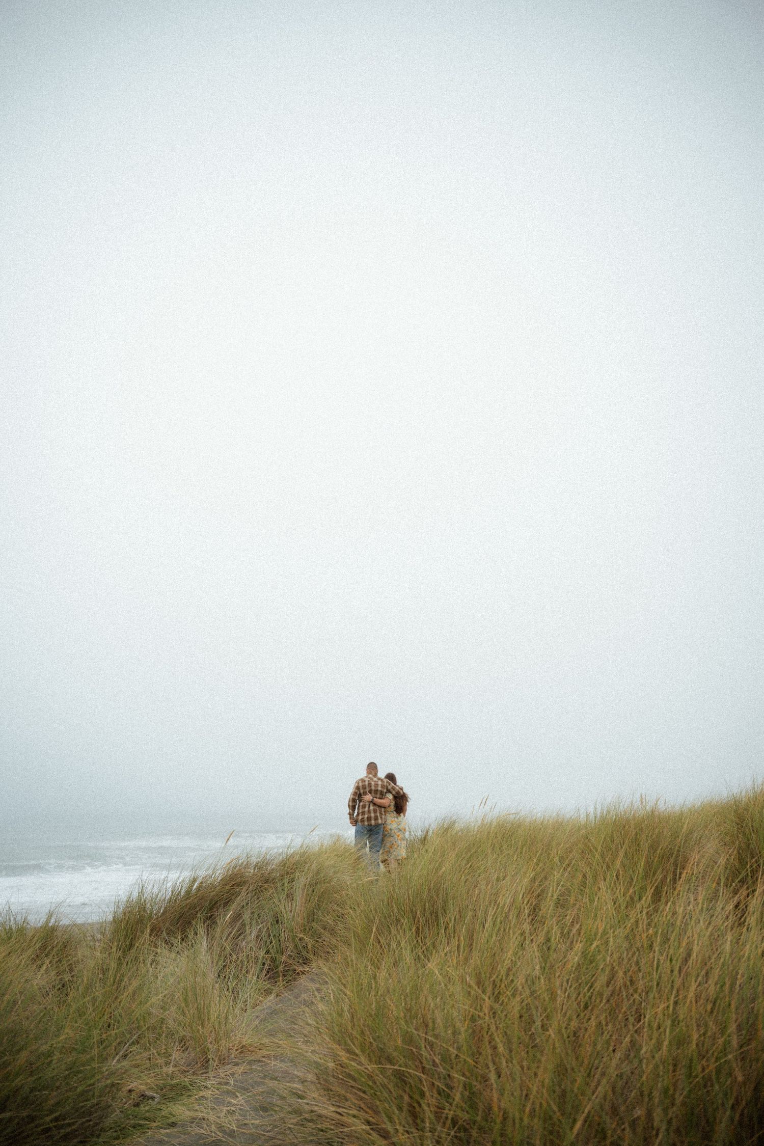 Distant figures walking through beach grass on a foggy coastal trail.