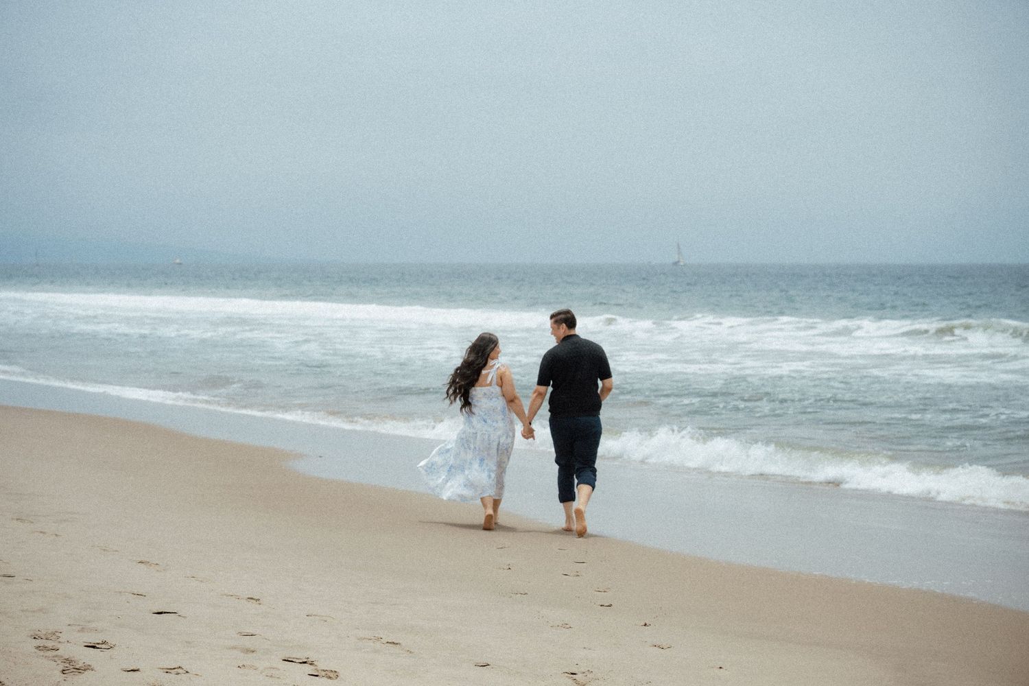 Two people walking along the shoreline of a beach with waves crashing.