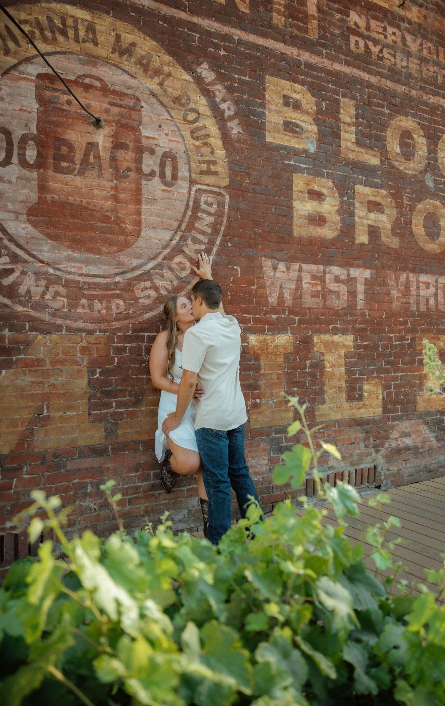 A romantic moment captured against an old brick wall with green foliage in the foreground.
