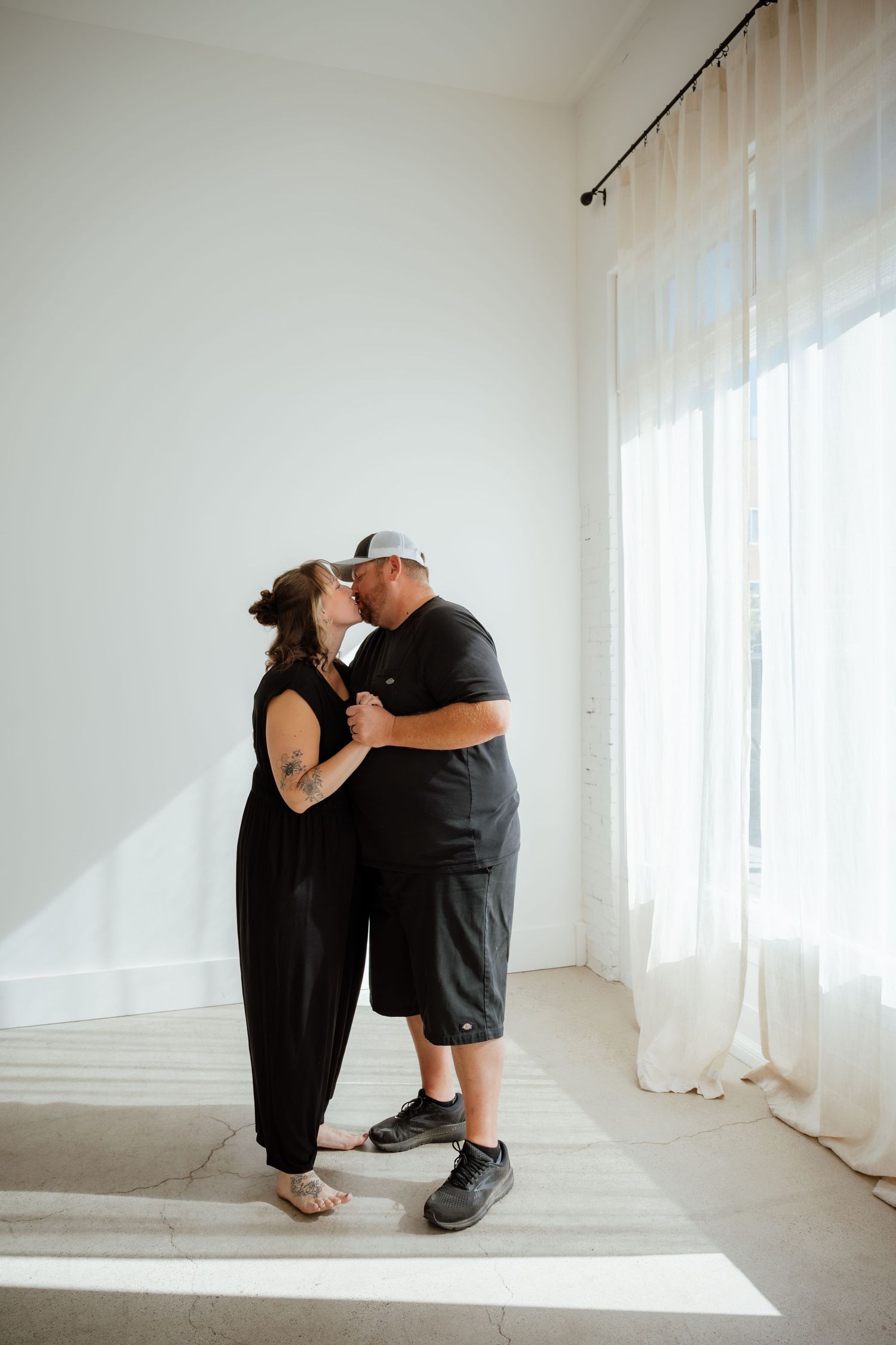 A couple dances together in a sunlit white room with sheer curtains.