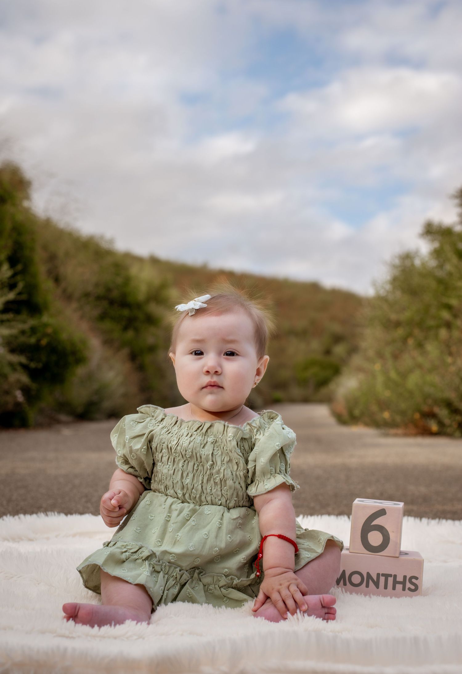 A baby in a mint green dress sits on white blanket with a 6 months milestone marker.
