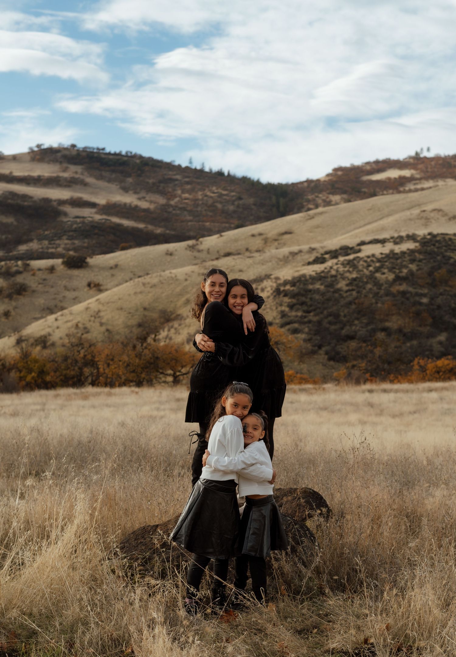Family shares tender moment in autumn field with rolling hills behind.