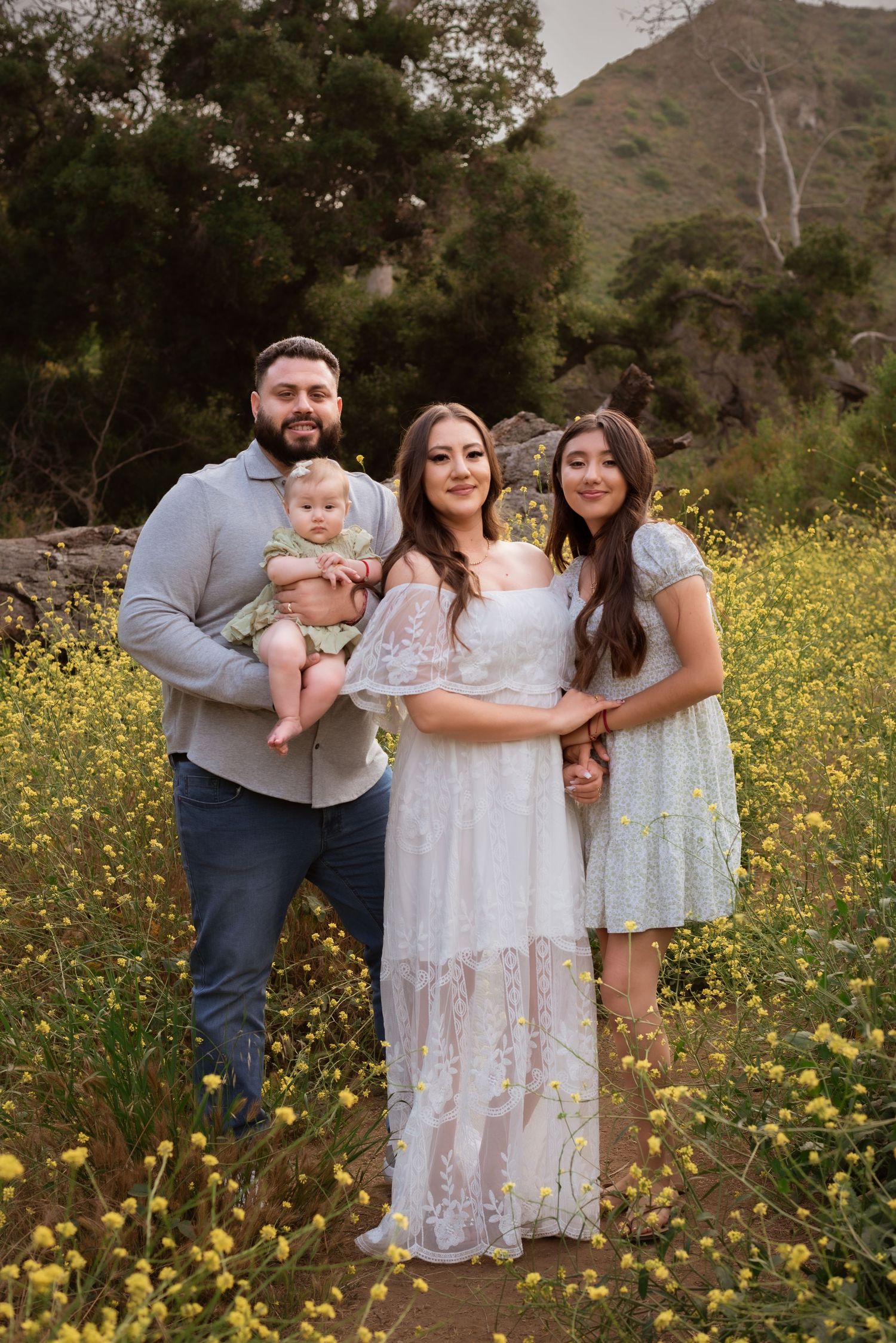 Family portrait in field of yellow wildflowers with mountains in background.