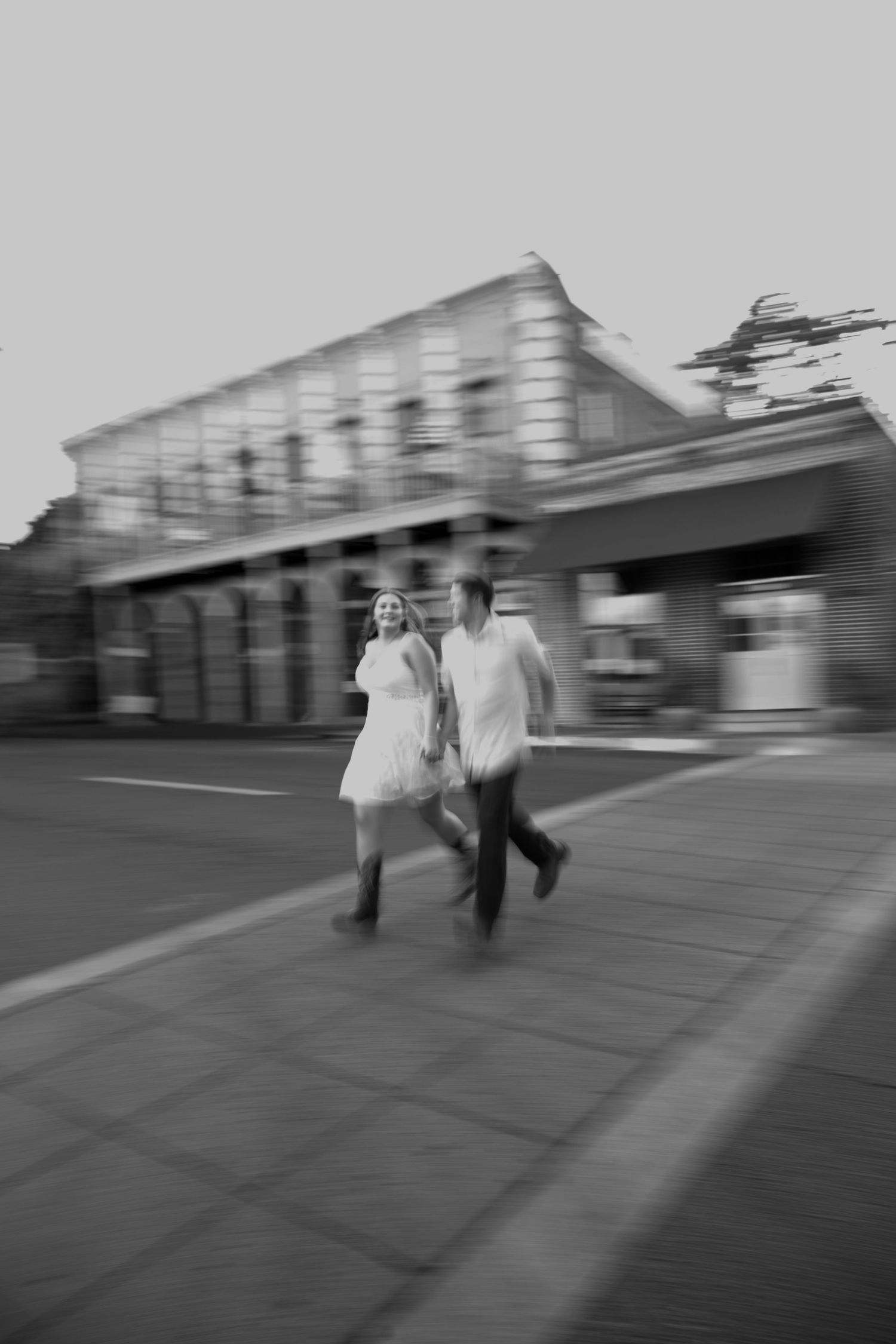 Motion-blurred sequence of a couple running together on a sidewalk.