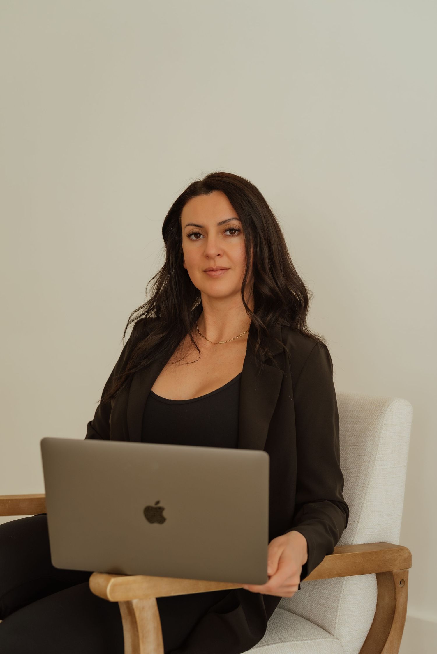 Woman working on laptop while sitting comfortably in wooden chair against white background.