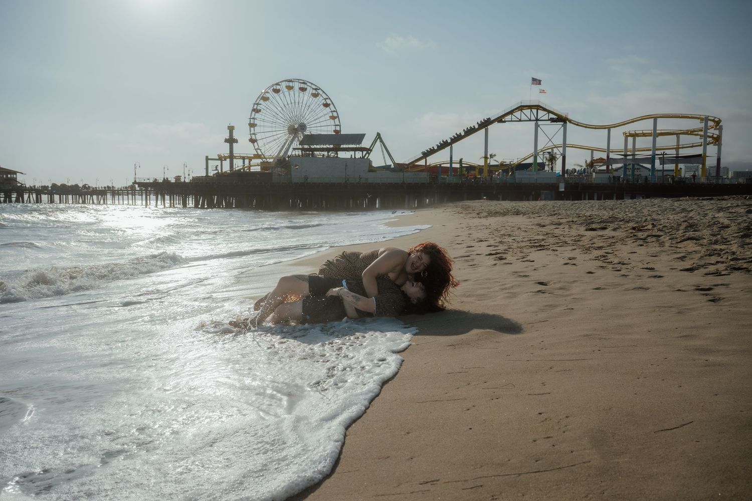 Panoramic beach landscape with pier, Ferris wheel, and rolling waves under cloudy skies.