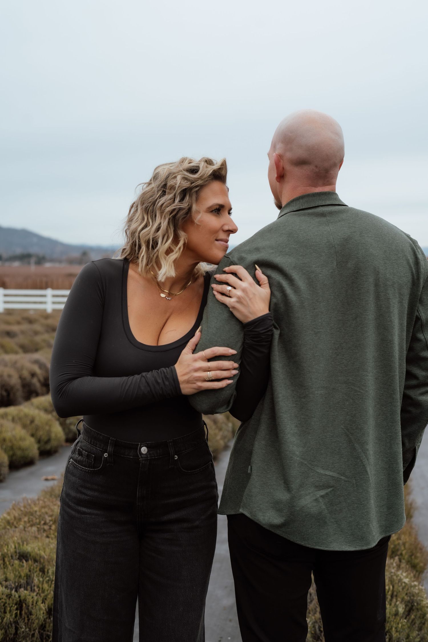 Couple in casual attire sharing tender moment against rural landscape background.