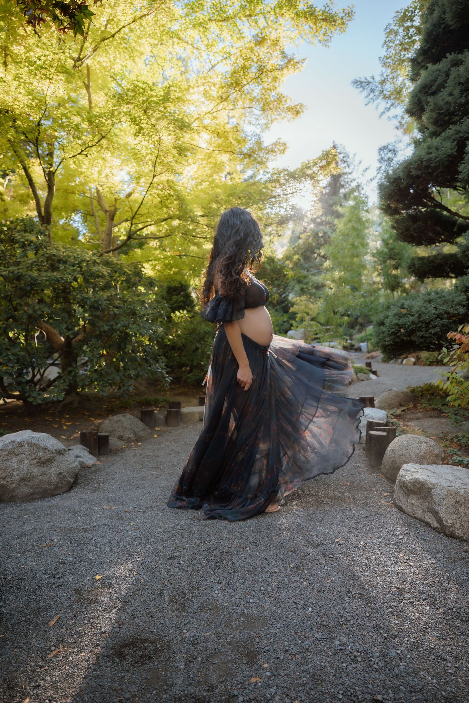 Person in flowing black dress twirls on forest path during golden hour.