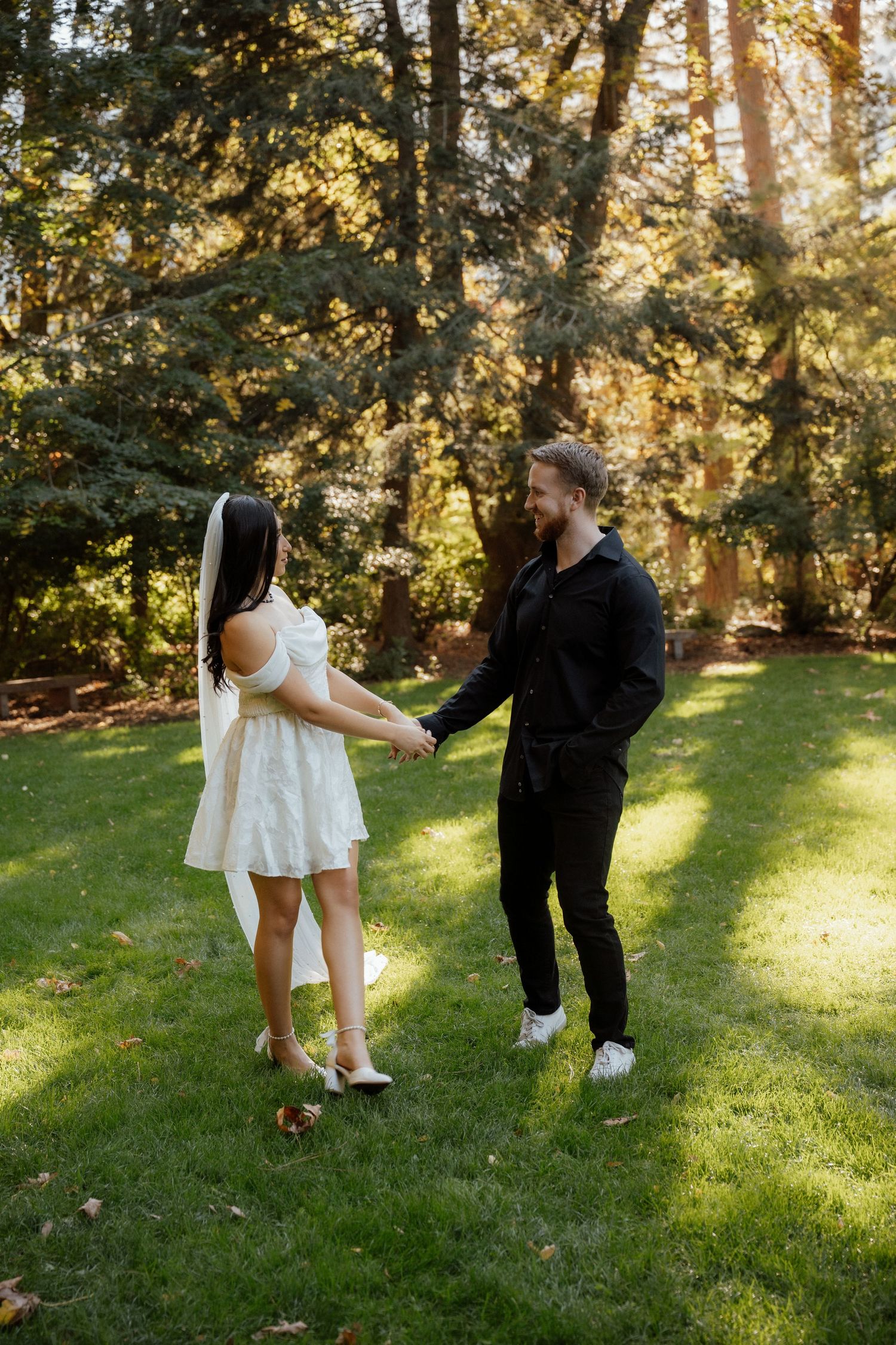 Playful couple in formal attire dancing on grass in golden afternoon sunlight.