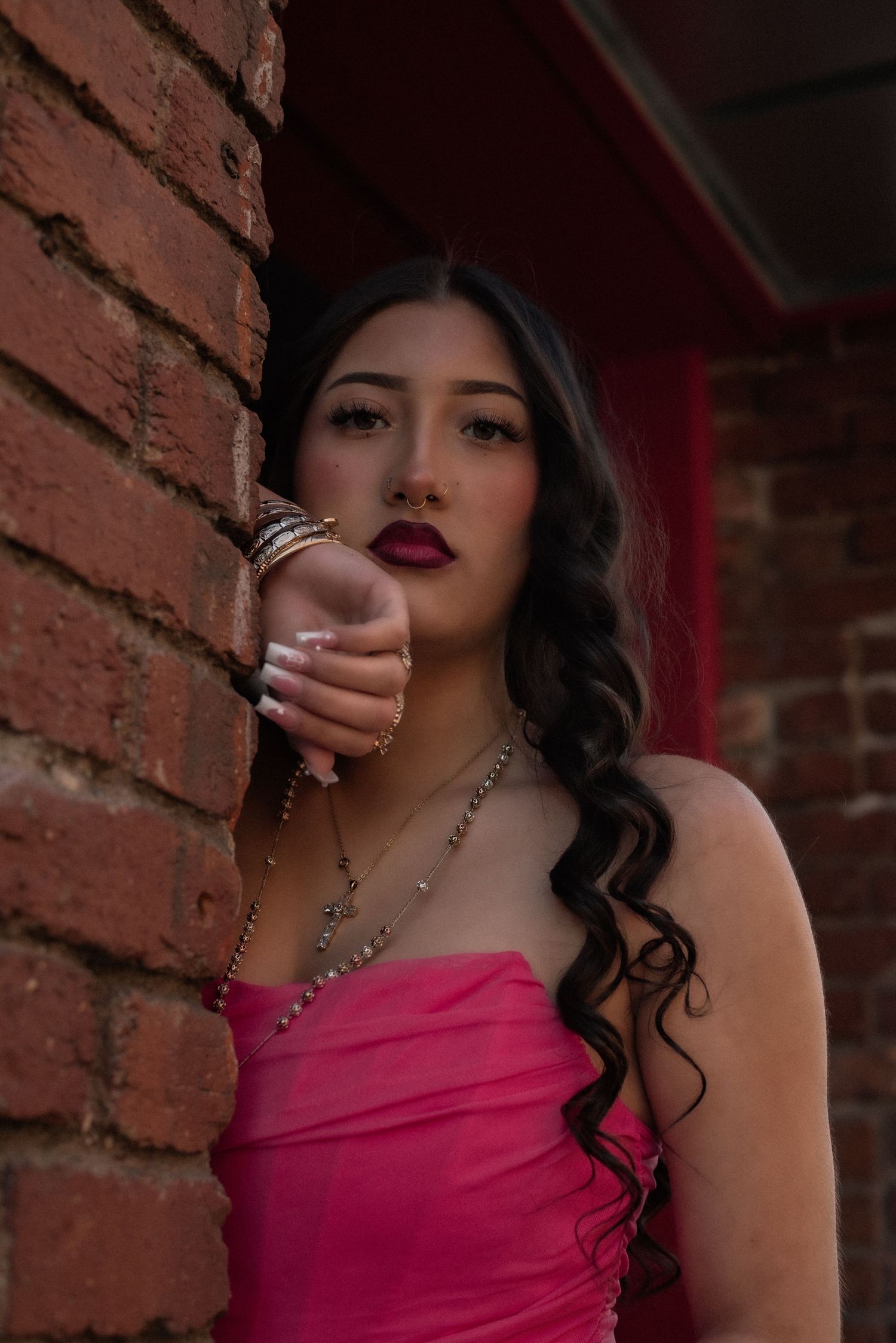 Dramatic portrait against brick wall with pink top and statement jewelry.